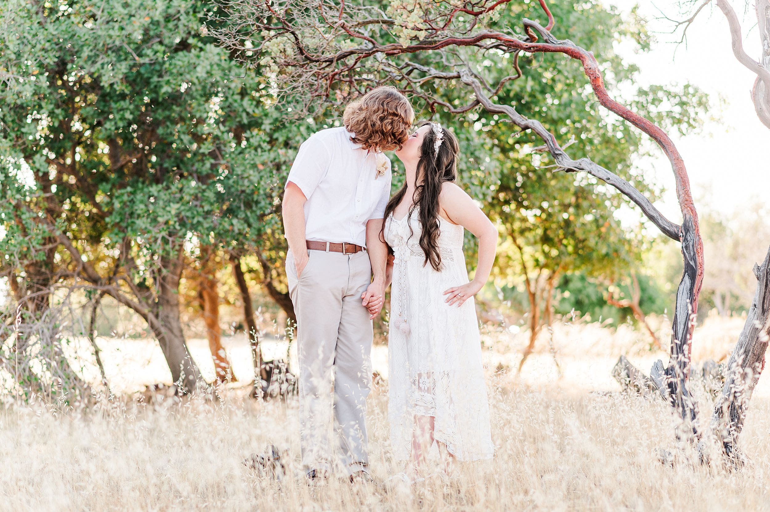 engaged couple sharing kiss with manzanita tree behind them