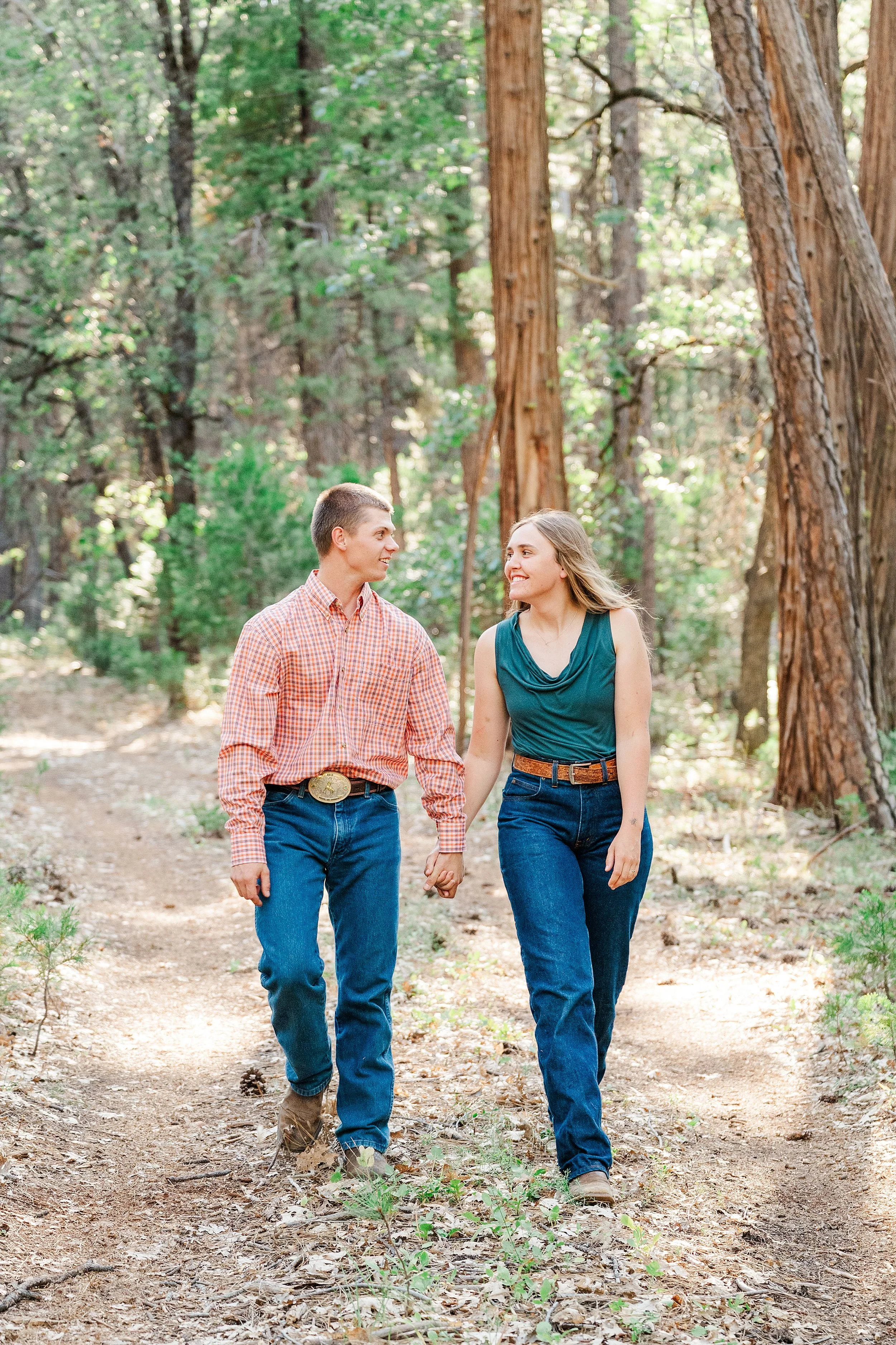 Romantic engagement portrait of a couple walking together through a sunlit forest in Whitmore, California.