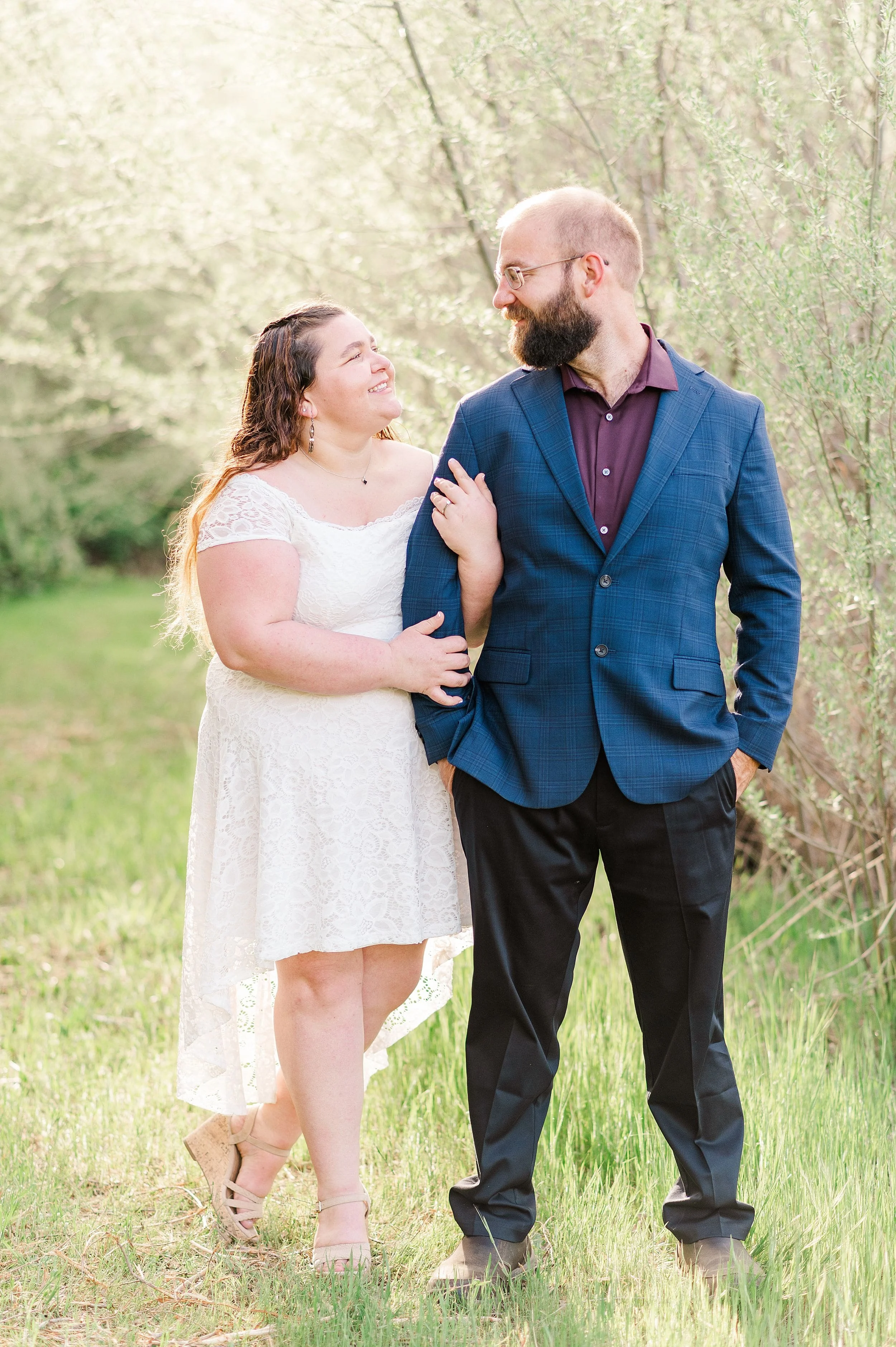 woman in white lace dress smiling at fiance wearing maroon shirt and navy blue suit coat