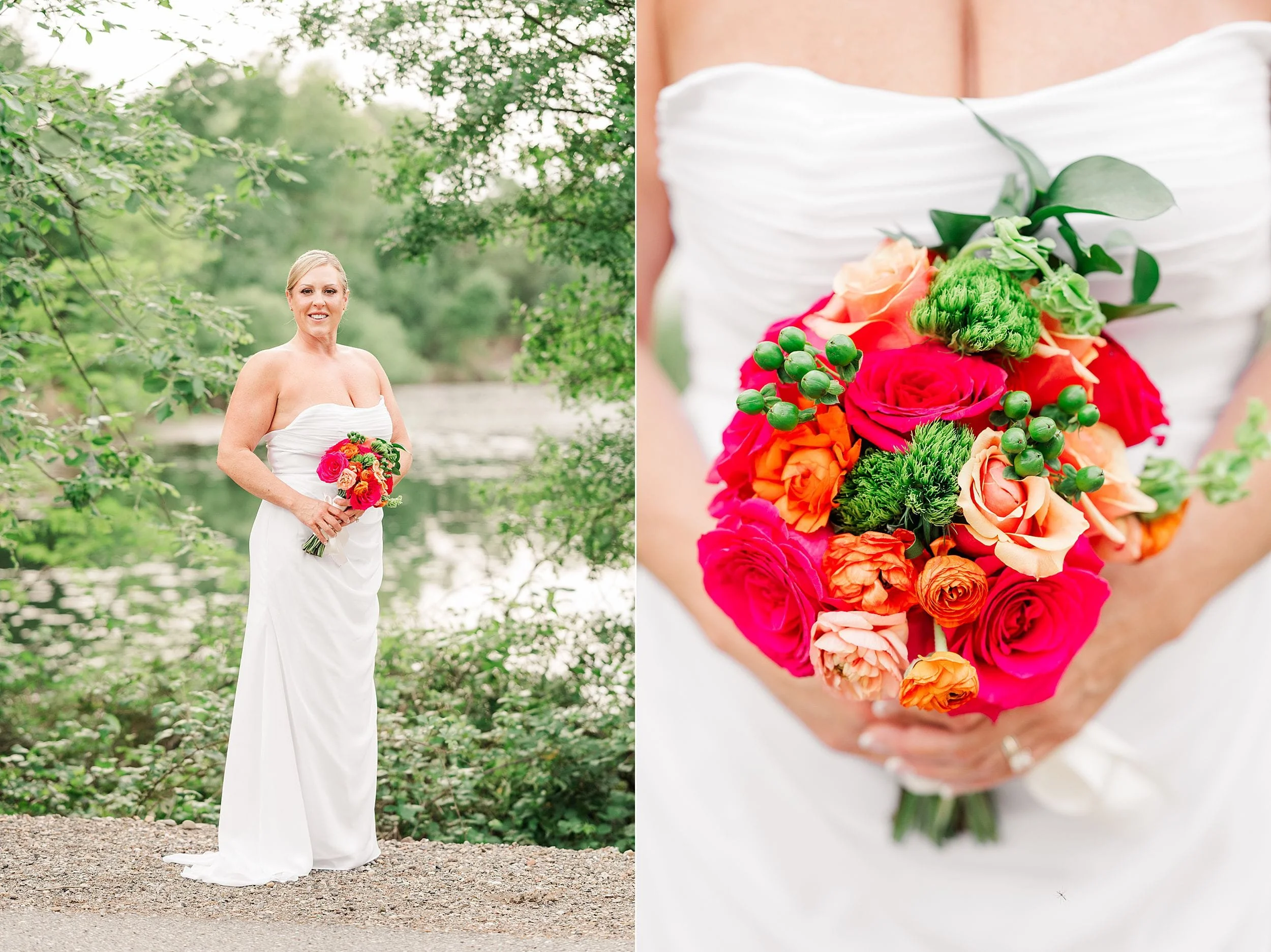 A bride in a strapless white gown holds a vibrant bouquet of red, pink, and orange flowers with green accents, standing by a serene, tree-lined lake.