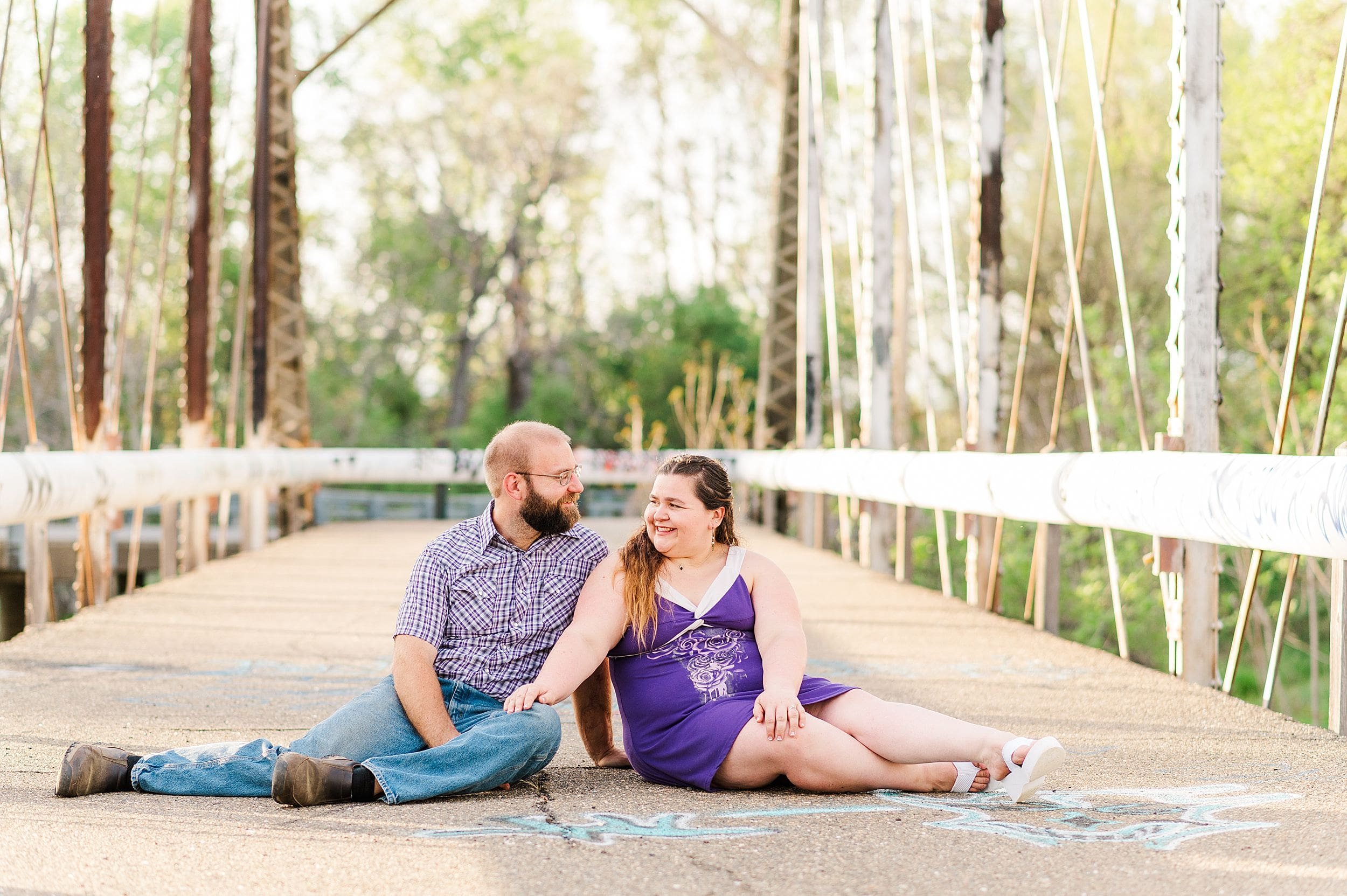 couple sitting on bridge smiling at each other in middle of bridge