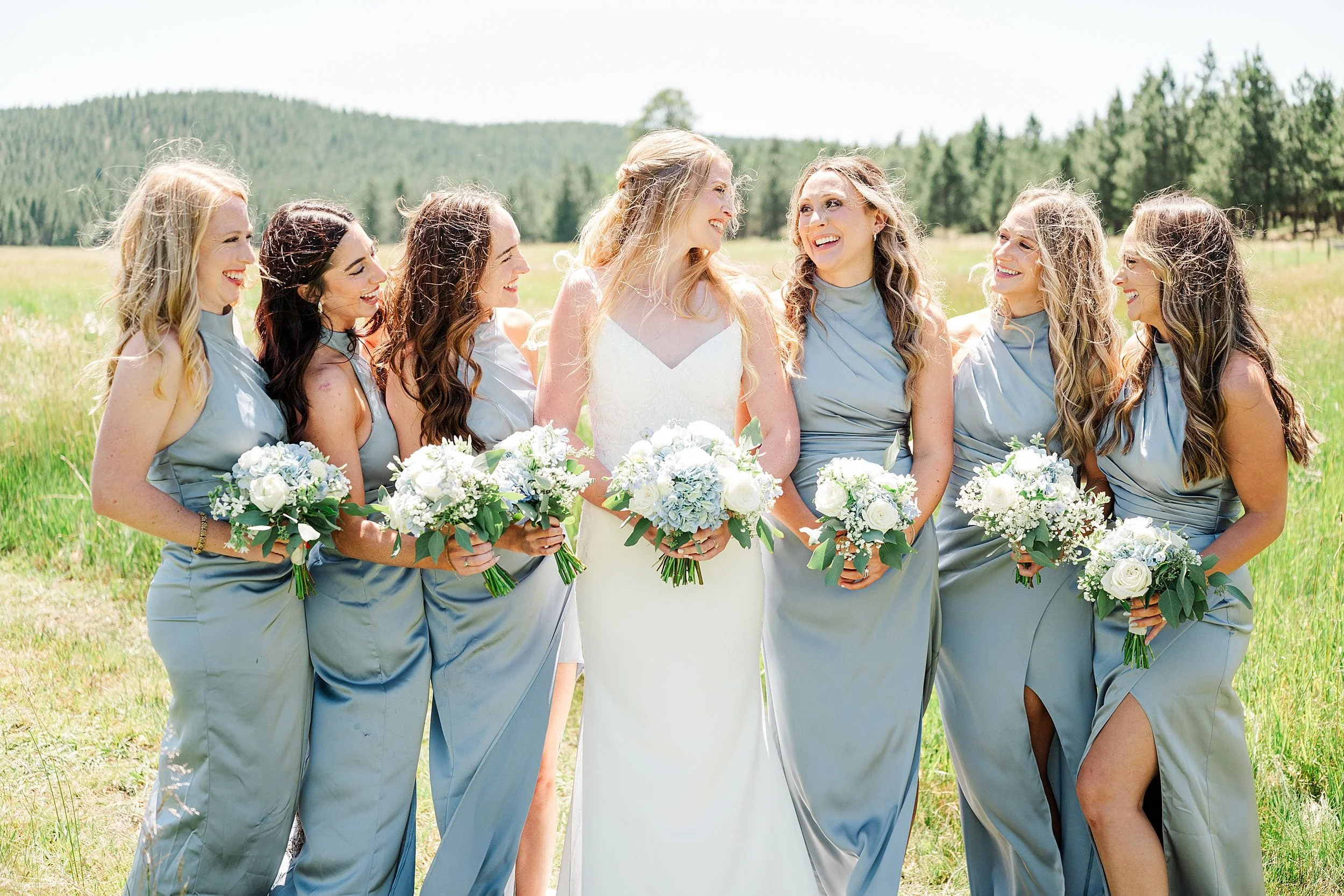 Bridesmaids in blue dresses holding white and blue bouquets at a ranch wedding.