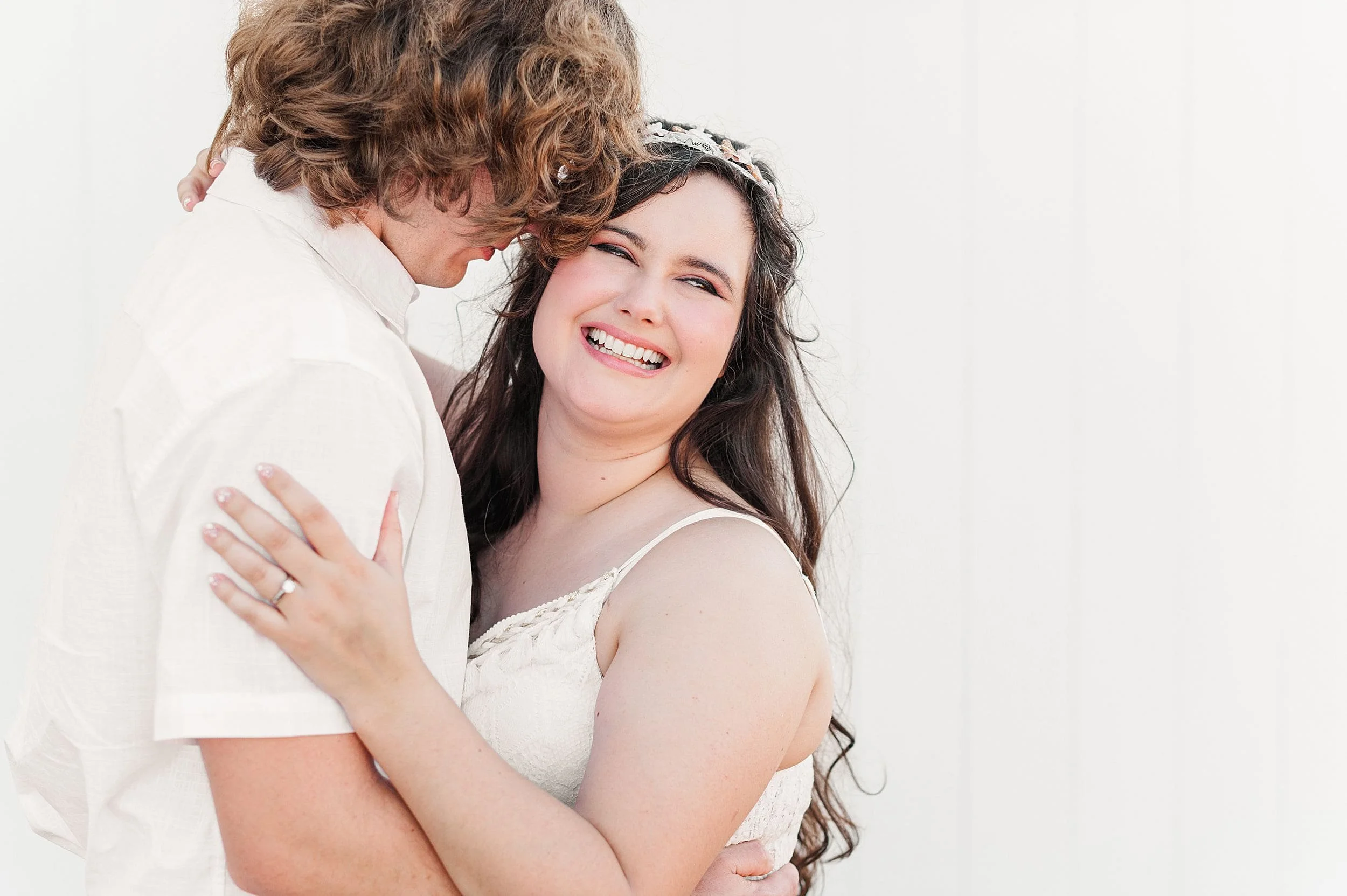 woman laughing over should with fiance nuzzled into her temple with white background