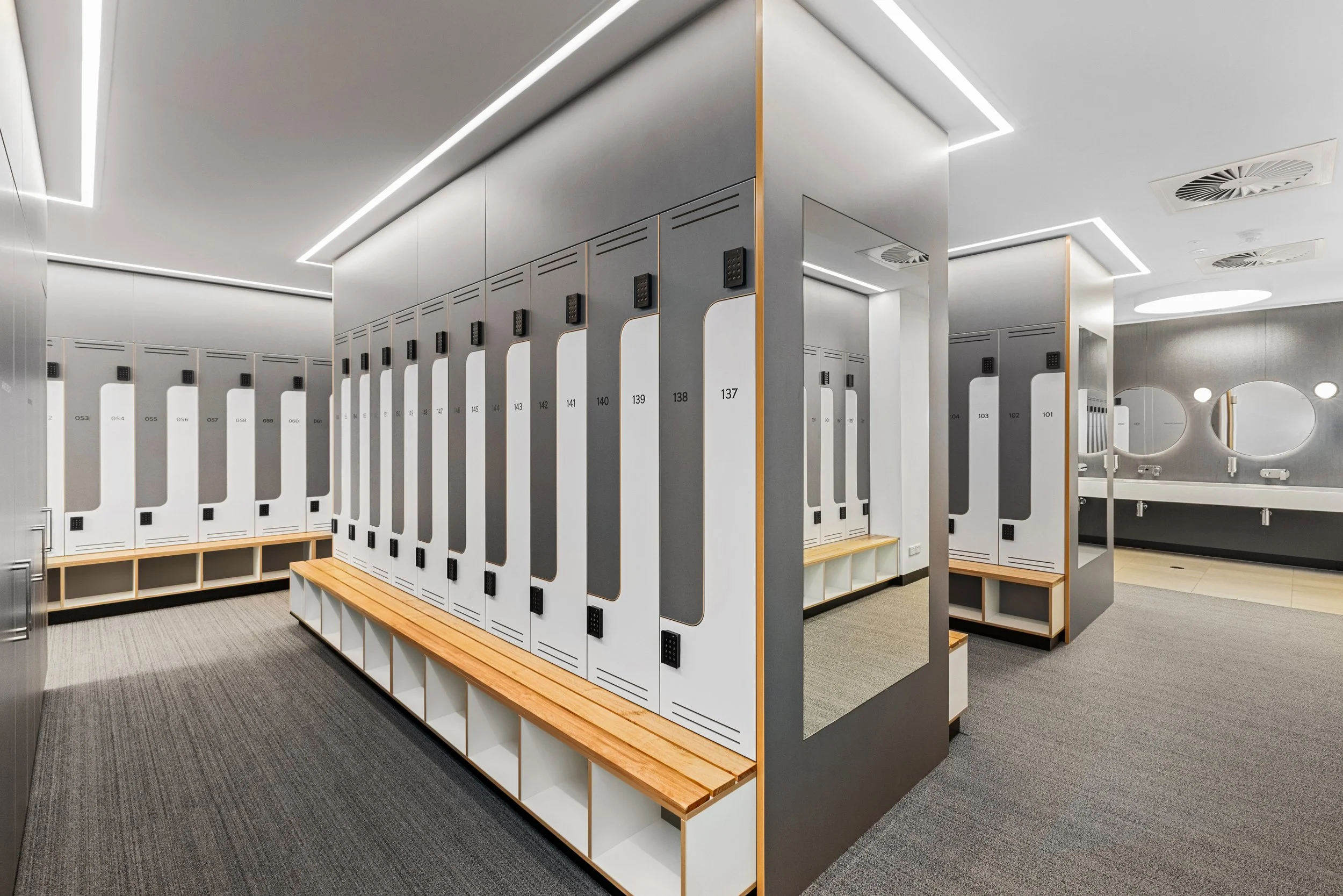 Modern locker room with numbered lockers, wooden benches, and circular mirrors on the wall, illuminated with sleek ceiling lights.