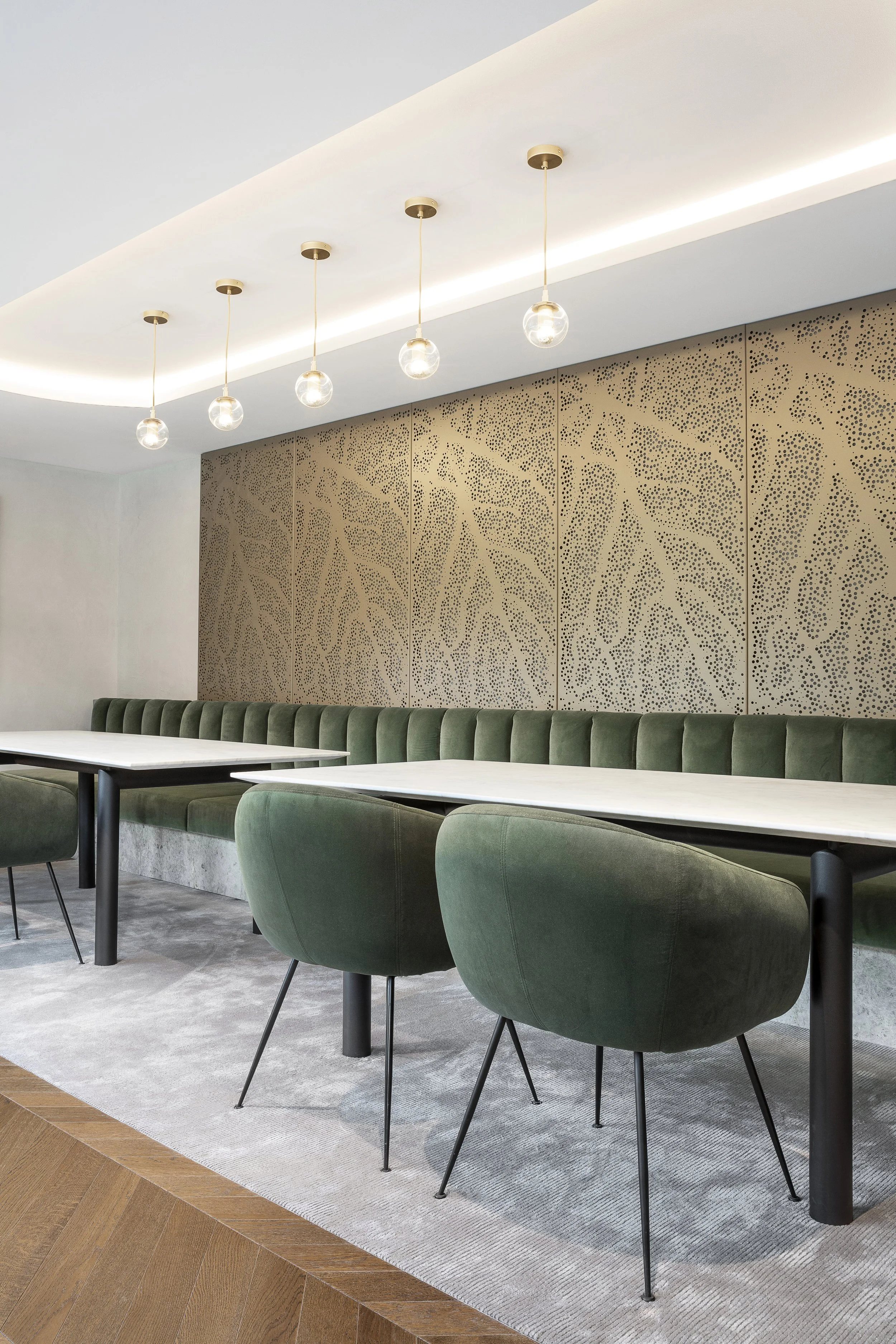 Interior of a modern dining area with green upholstered chairs, white tables, a textured beige wall panel, and modern pendant lights hanging from a curved ceiling.