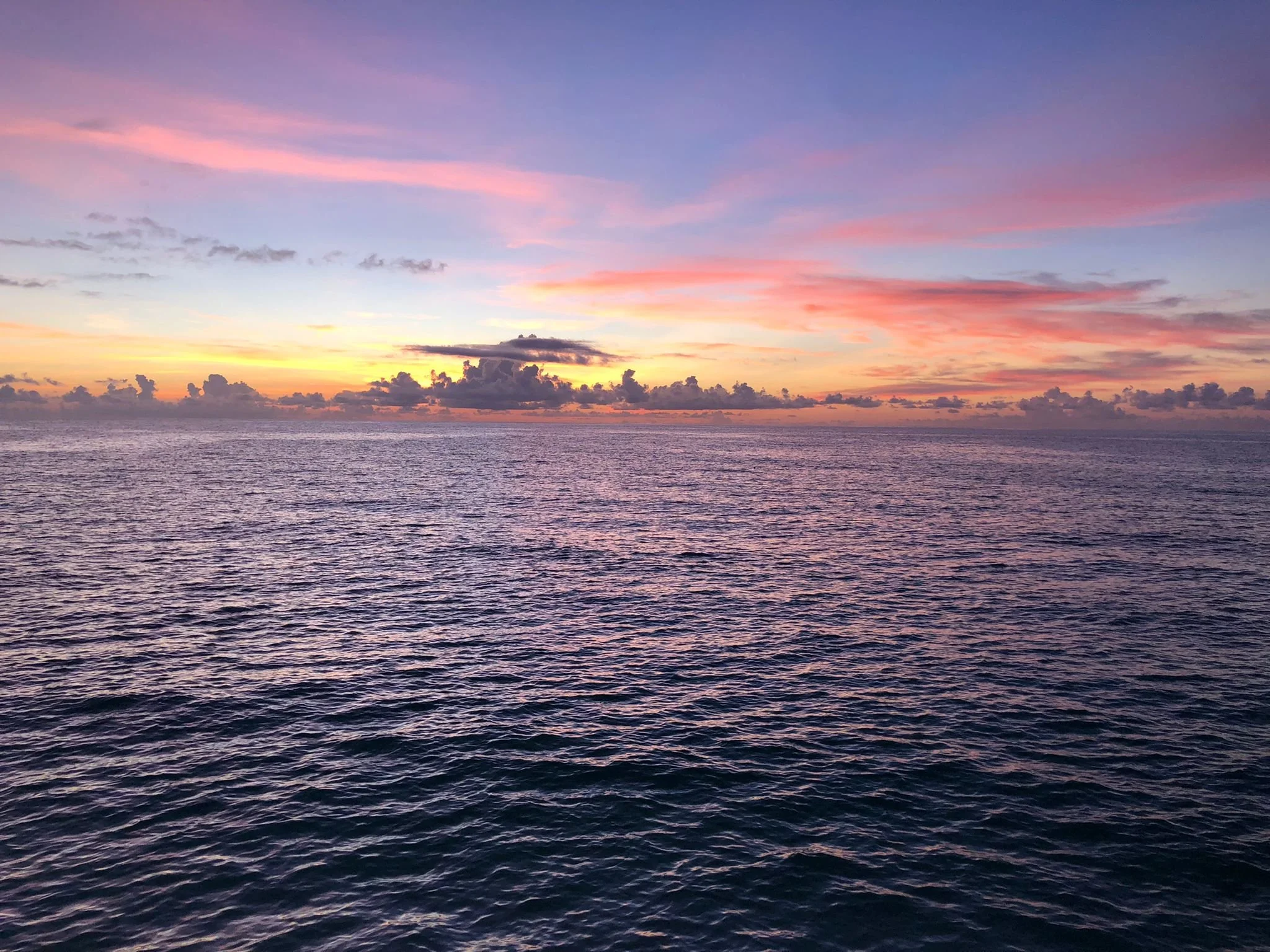 Sunset over ocean with colorful pink, purple, and orange sky and calm water surface.