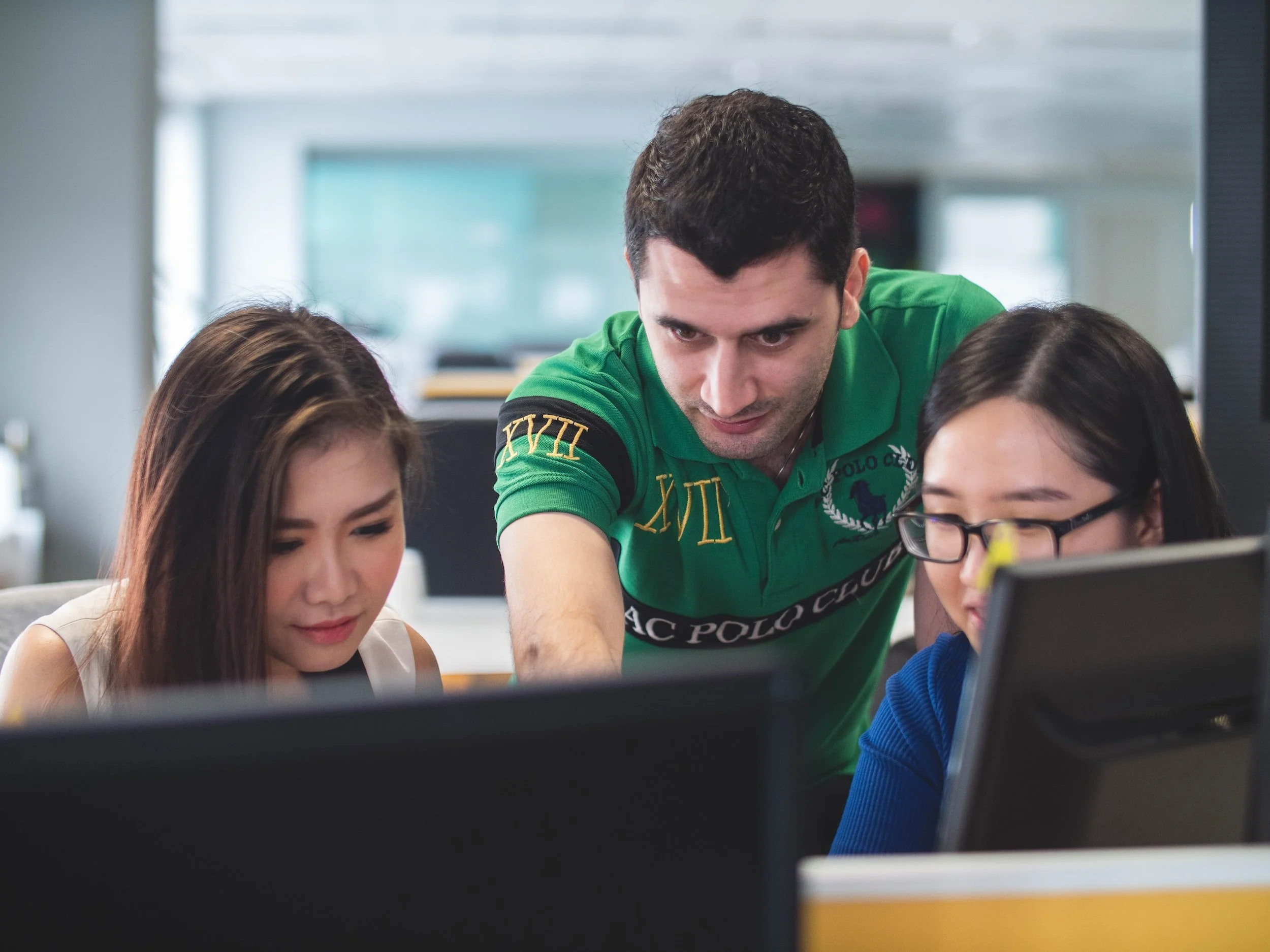 a person pointing to a computer screen as two others follow along