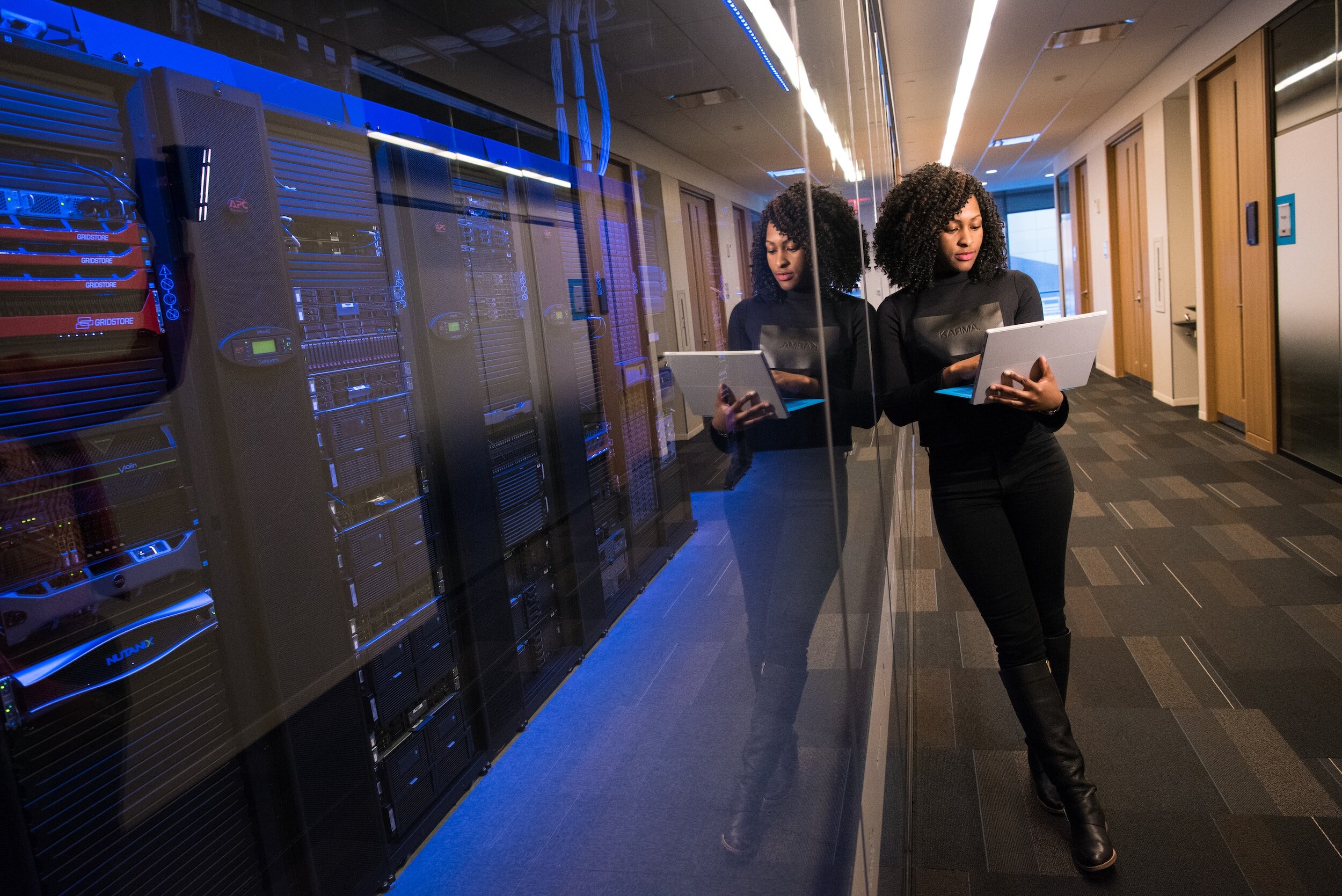 a person on their laptop leaning against the glass for a room with many large computers
