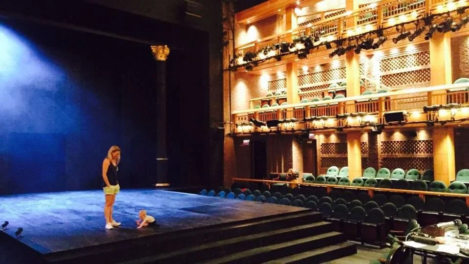 A young woman and a baby on a stage in an empty theatre
