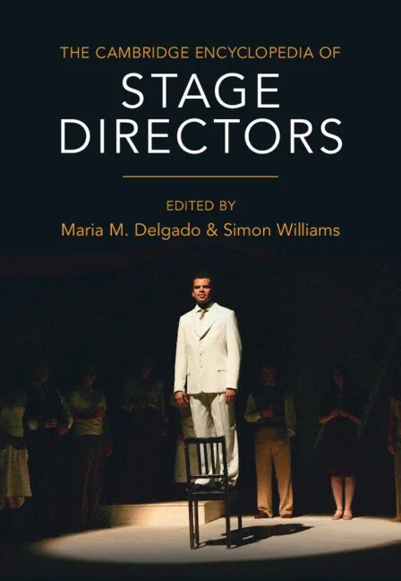 Cover of the Cambridge Encyclopedia of Stage Directors showing a man in a white suit standing on a chair in a spotlight that is fringed by shadowy figures