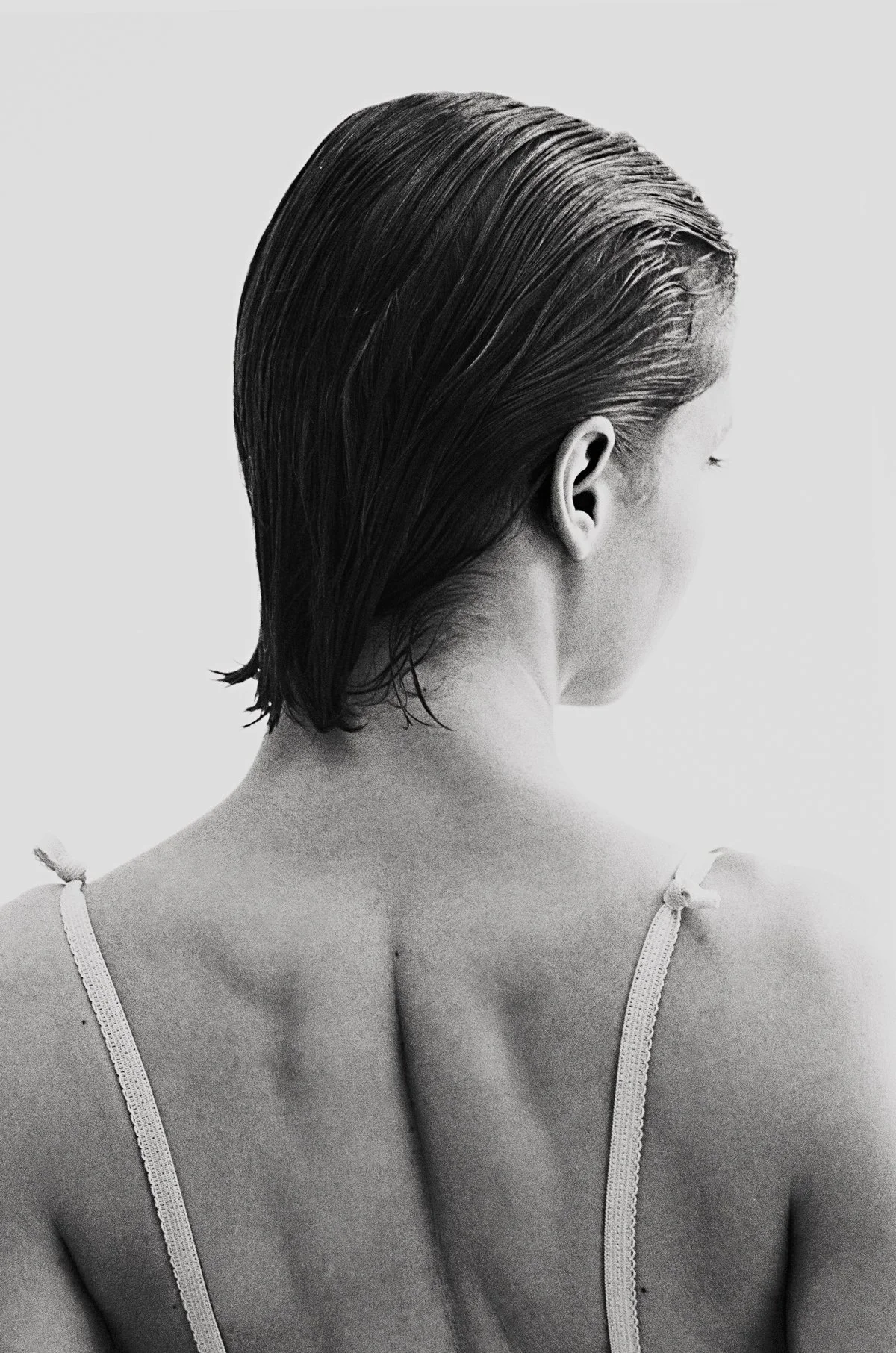 Schwarze nasse Haare einer Frau, frontal von hinten, in Schwarz-Weiß-Aufnahme, ohne Gesicht sichtbar, nur Nacken und Schultern, in Unterwäsche. minimalistisches Porträt.