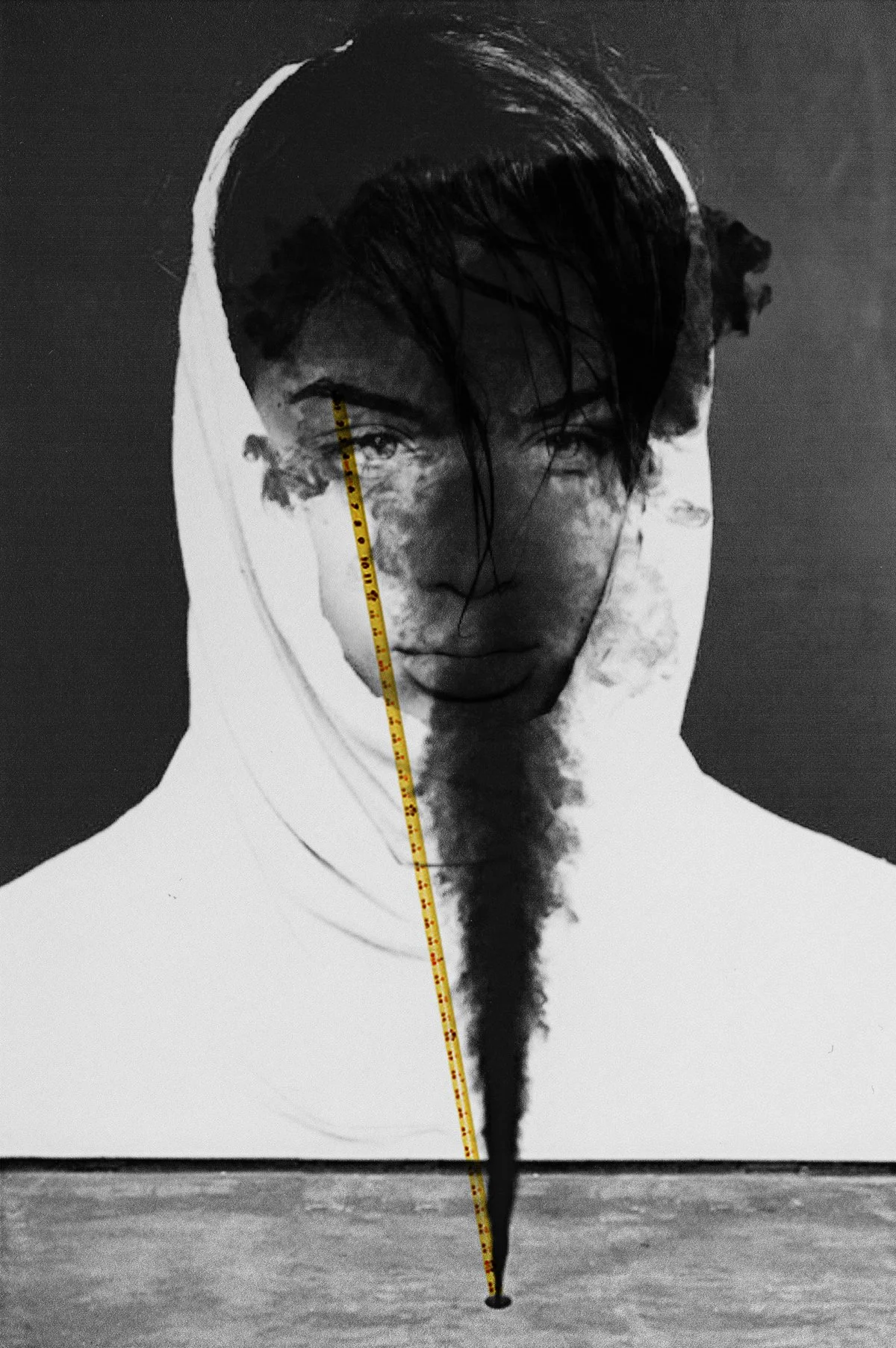 Schwarz-Weiß-Fotografie eines männlichen Gesichts mit dunklen, nassen Haaren und Hoodie, mit einer Messlatte, die auf das Gesicht zeigt, vor einer Landschaft mit Wasser. Der obere Teil des Bildes ist vom Gesicht, der untere Teil vom Wasser. Es handel