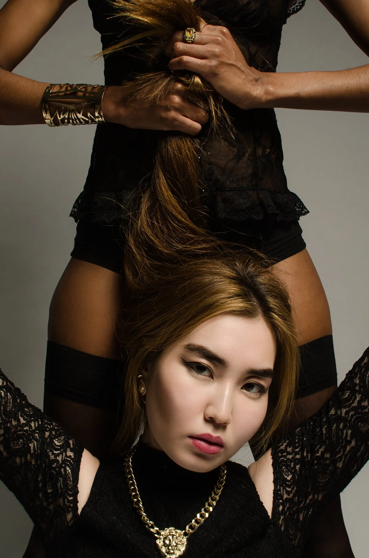 Zwei Frauen in schwarzen Outfits, schöne dunkle Haare, tragen Goldschmuck, eine mit langen Haaren, pose bei einem Fotoshooting, moderne Mode, stilvoll.