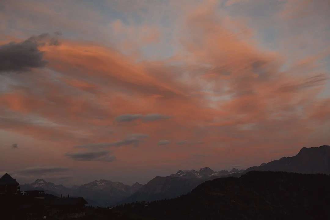 Blick auf Berge bei Sonnenuntergang mit orangefarbenen Wolken am Himmel.