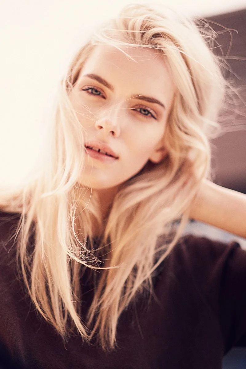 Nahaufnahme einer blonden Frau mit lockigem Haar, die an die Kamera schaut.