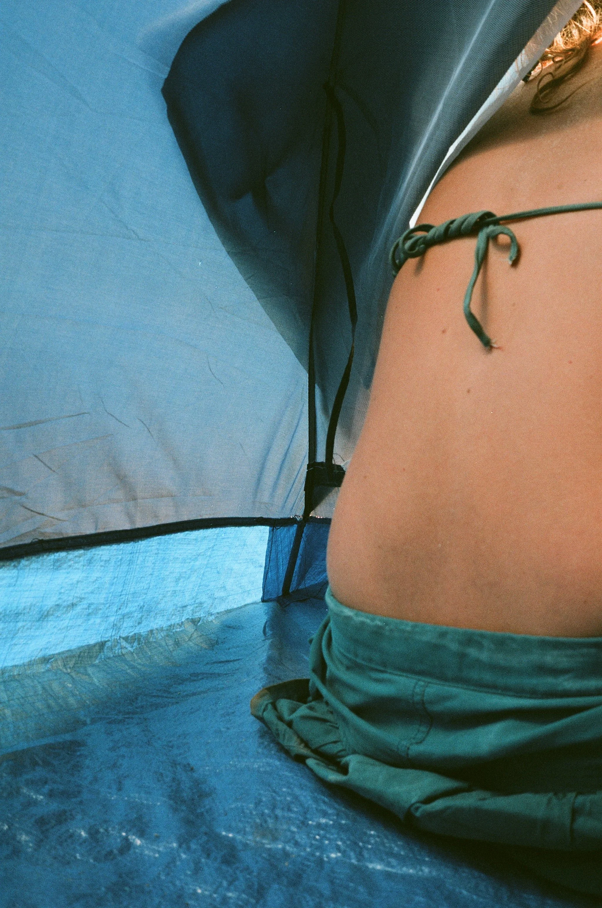 Person sitzt in einer blauen Zeltkuppel, trägt graue Shorts und ein dunkles Oberteil, die Blickrichtung ist nach vorne gerichtet, und nur ein Teil des Oberkörpers ist sichtbar.
