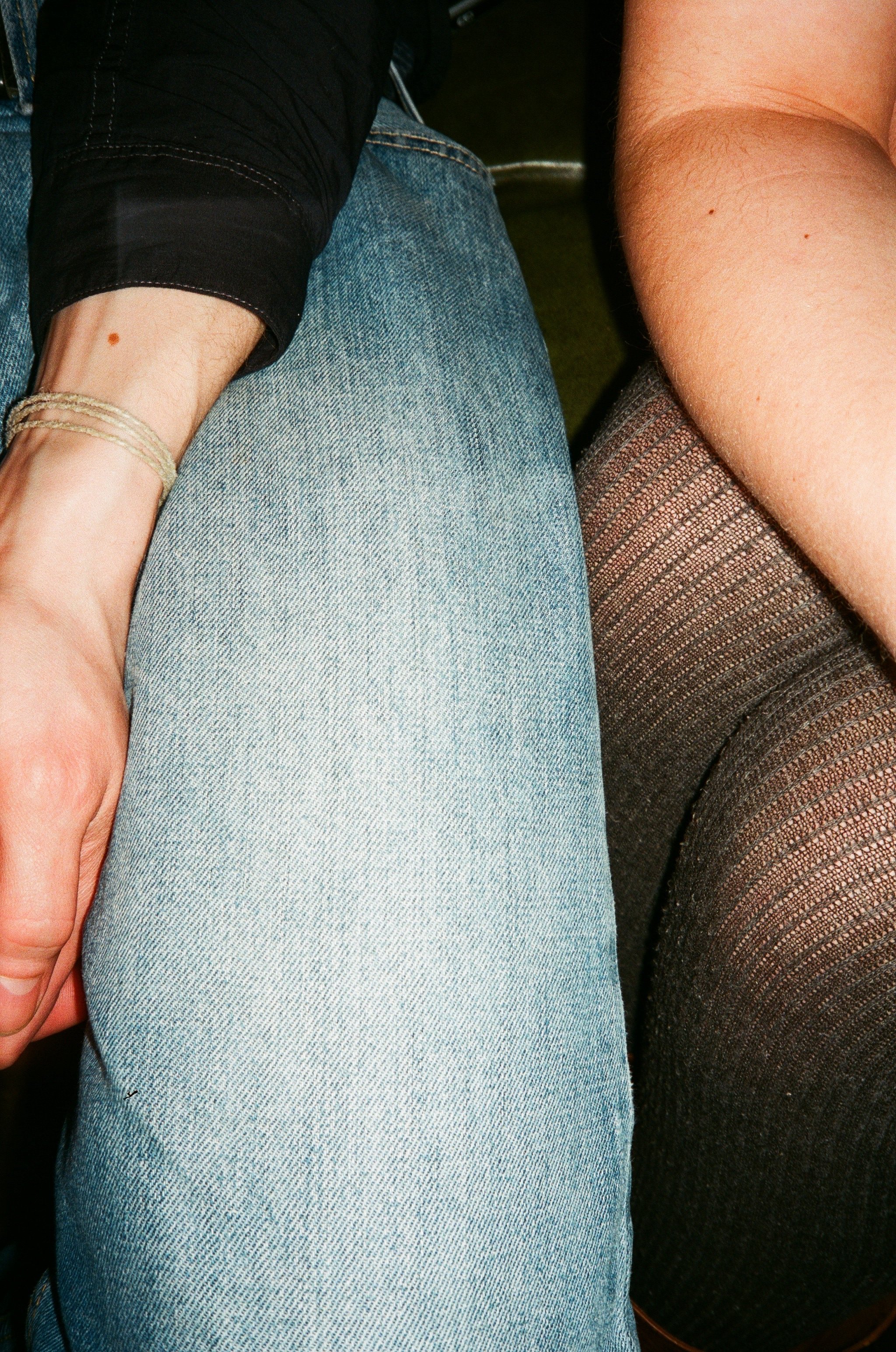 Nahaufnahme von zwei Personen, eine trägt hellblaue Jeanshose, die andere schwarzen Netzstrumphose. Eine Person hat eine goldene Armbanduhr am Handgelenk.