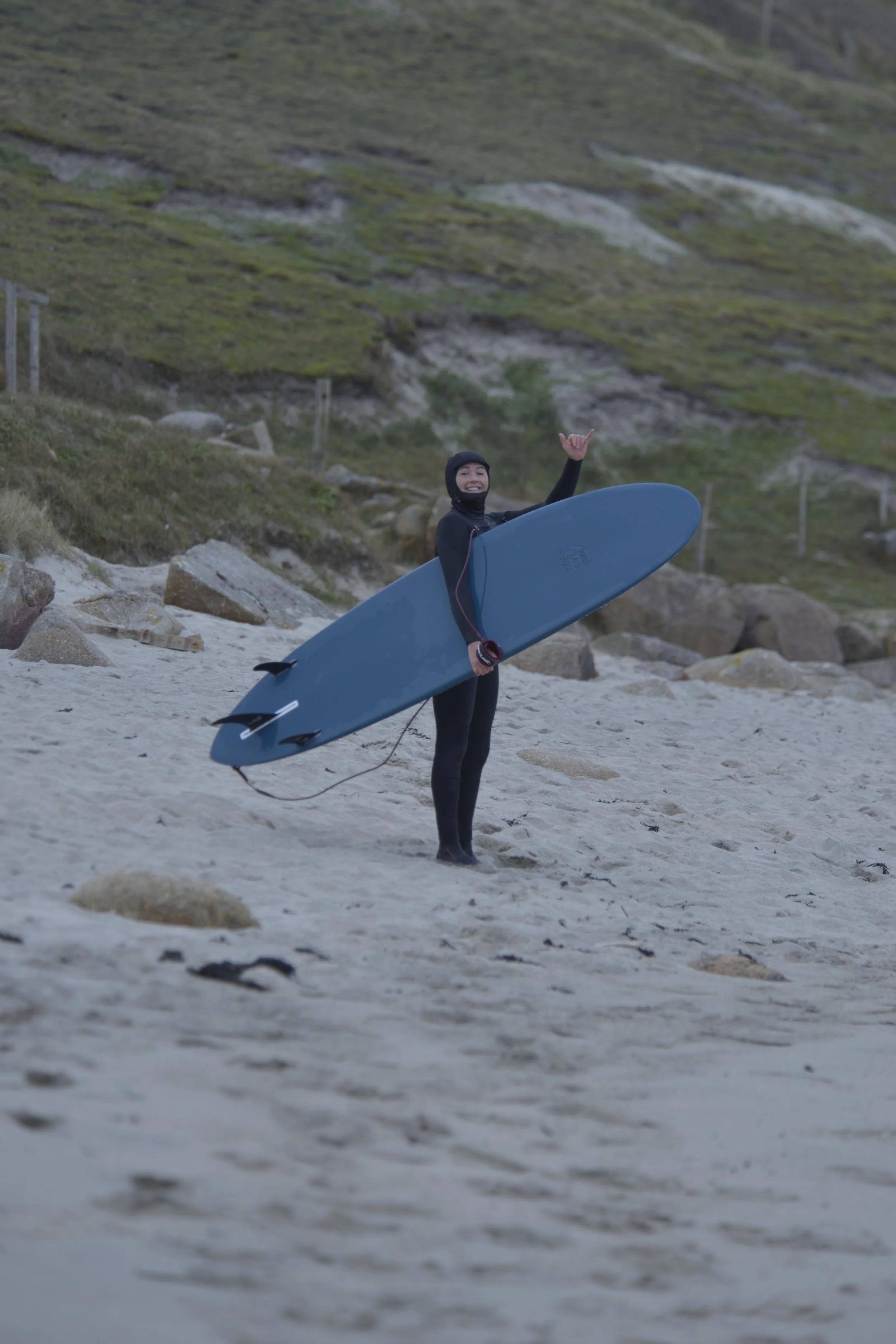female surfer holding a mini-mal surfboard on a Cornish beach