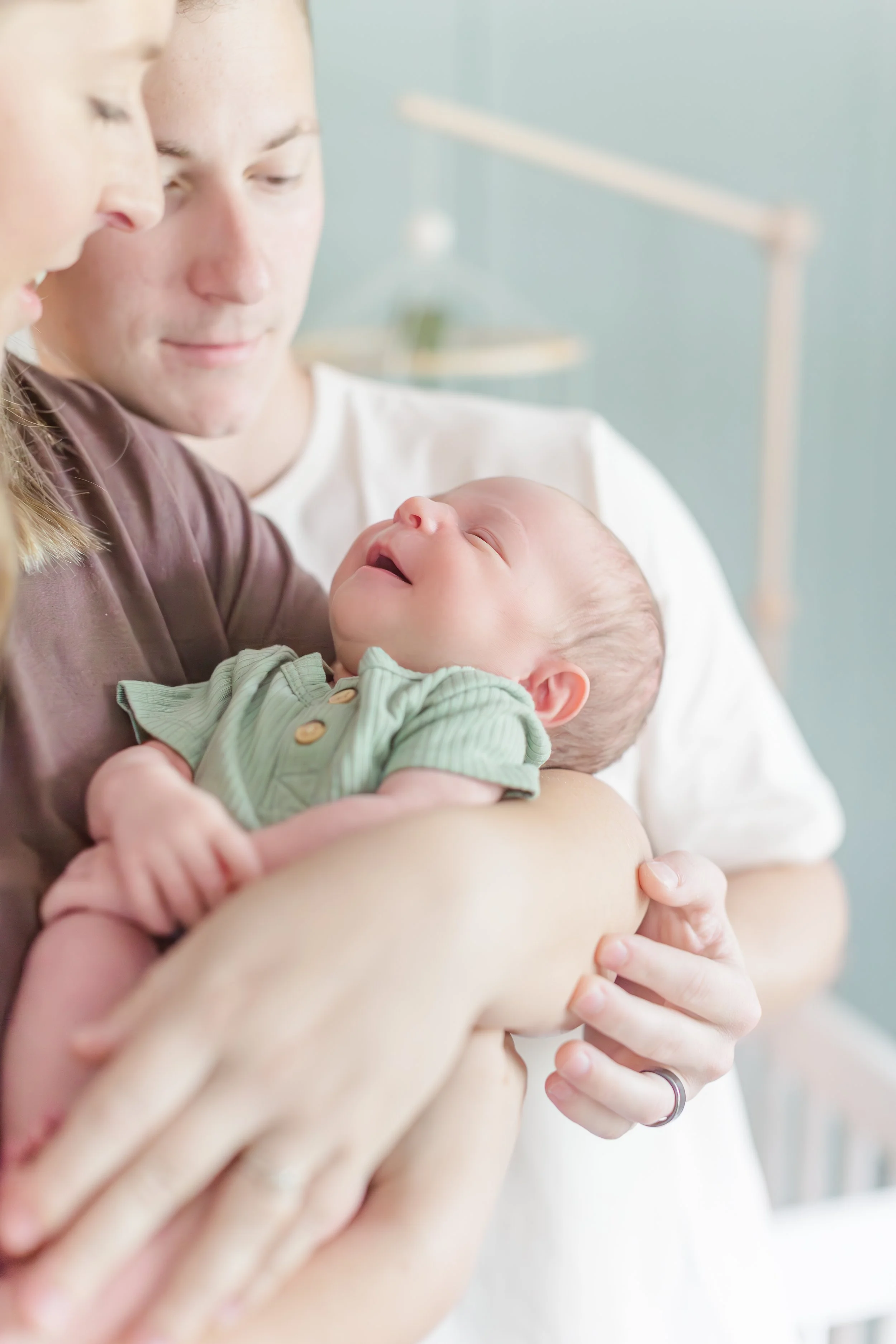 Newborn baby wearing a green outfit being cradled by two adults.
