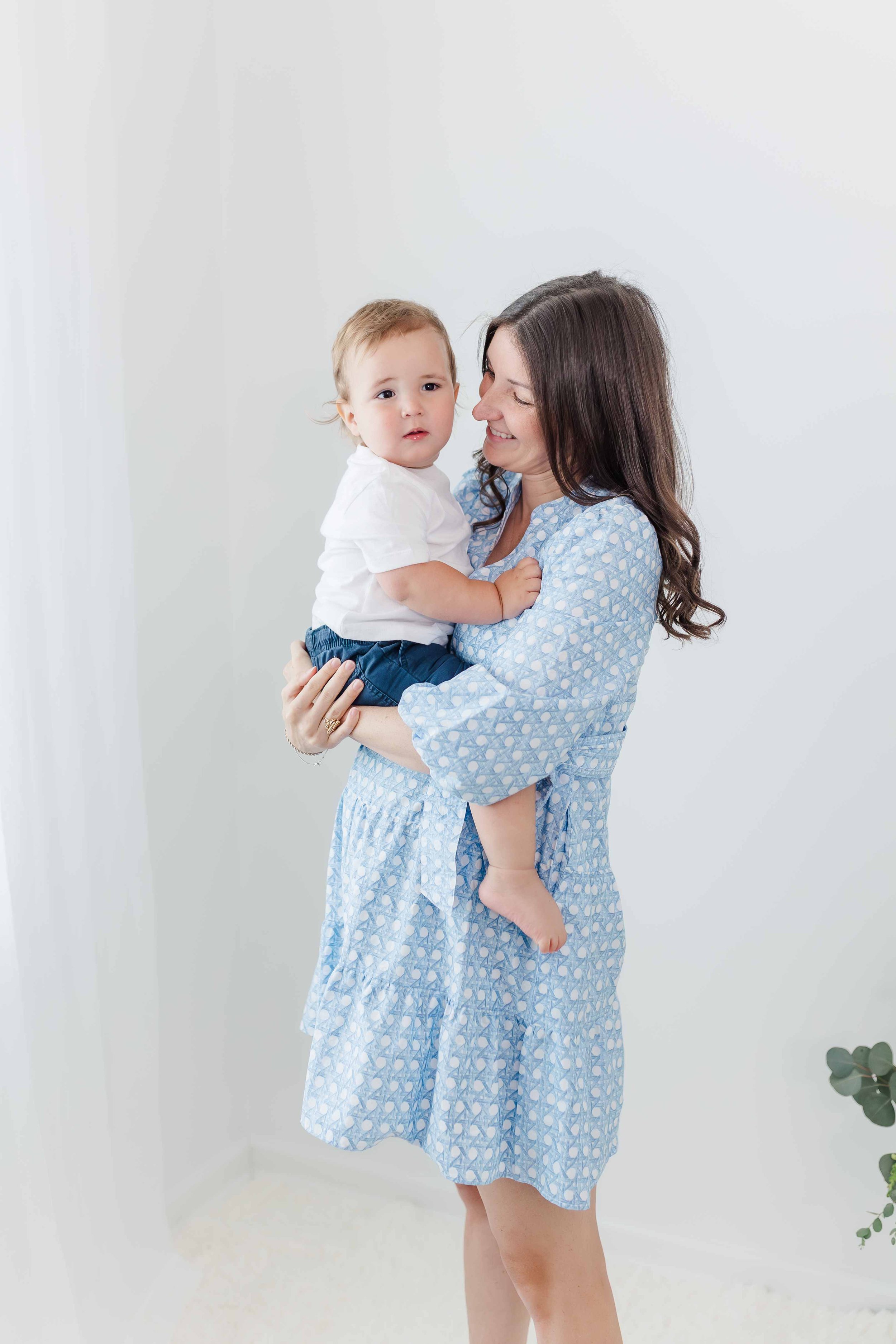 Mom in blue dress laughing with baby during studio milestone session in Greenville SC