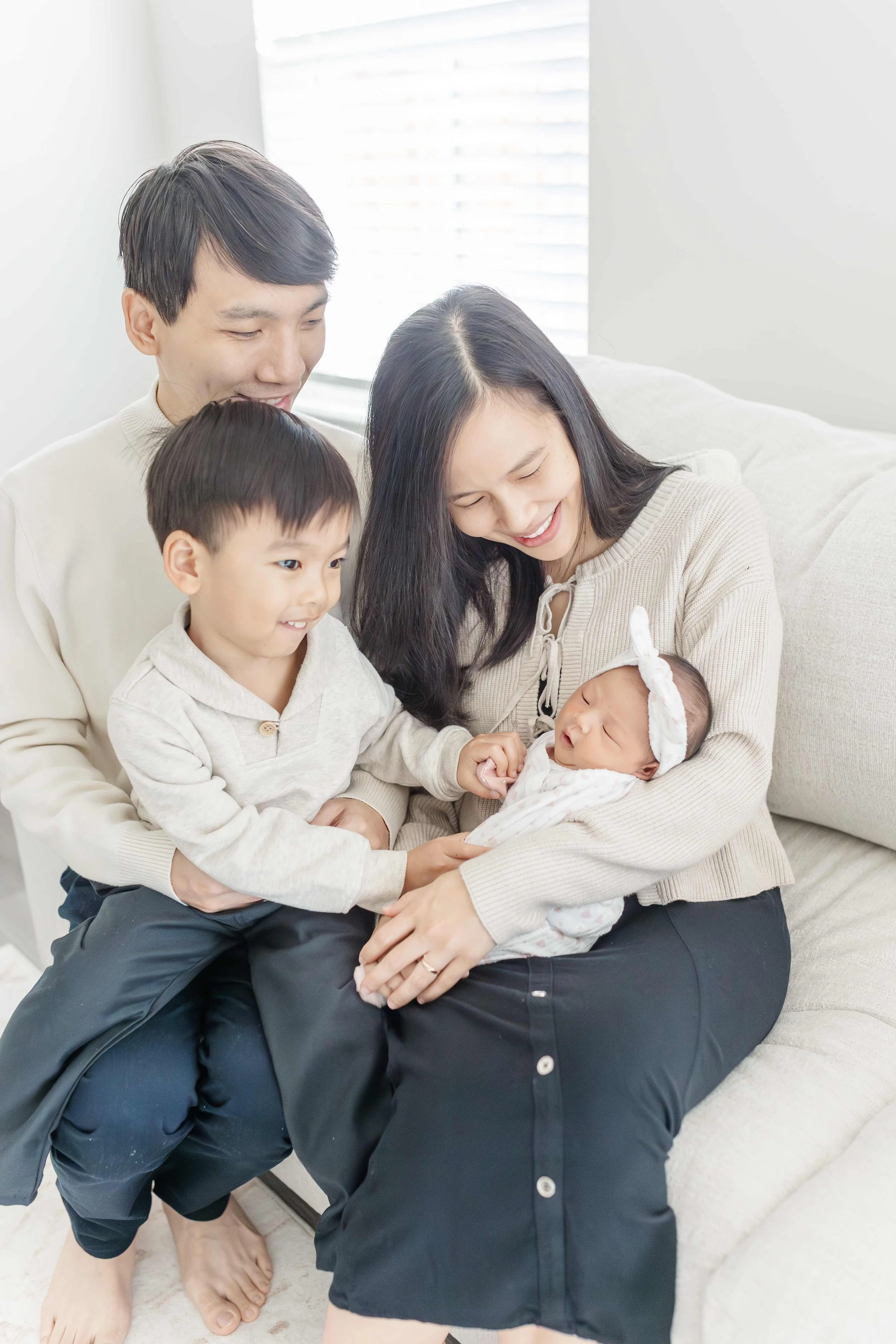 Mom holding newborn baby while toddler son sits beside her on a cream couch — Greenville South Carolina newborn photography