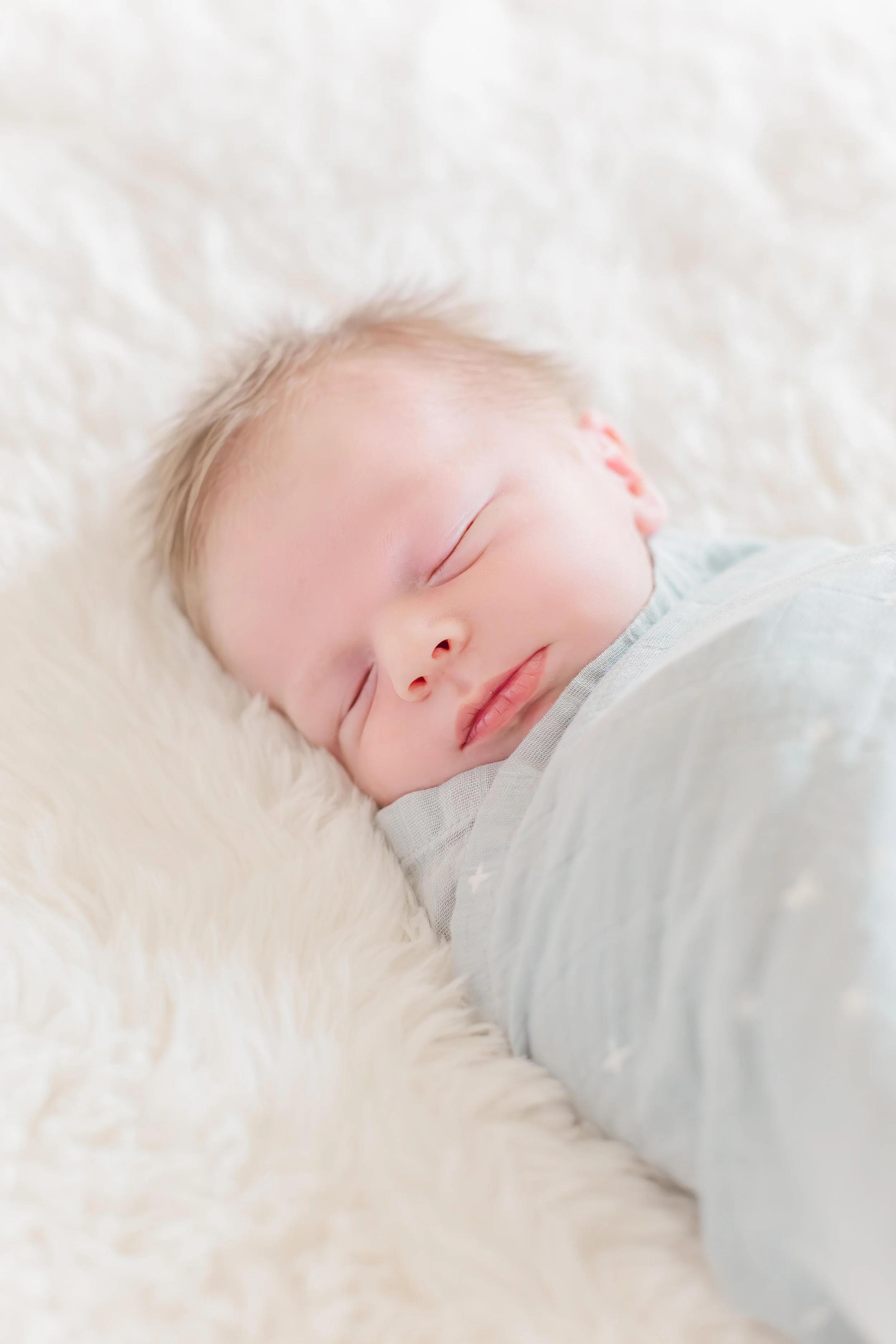 A sleeping baby with fair skin and light hair, lying on a plush white blanket in lifestyle family photoshoot in greenville south carolina