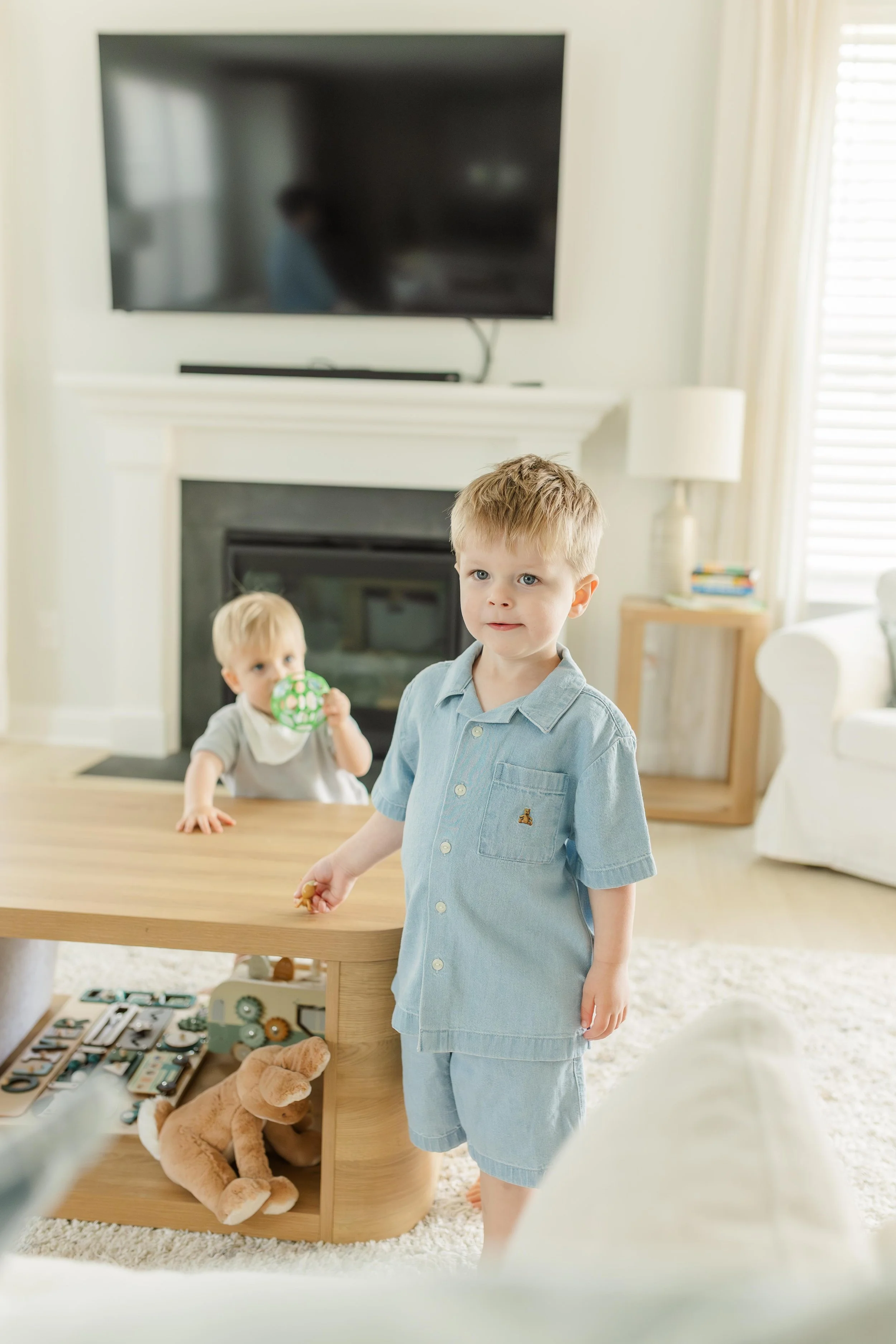 Toddler boy in blue romper standing in living room during in-home lifestyle family session