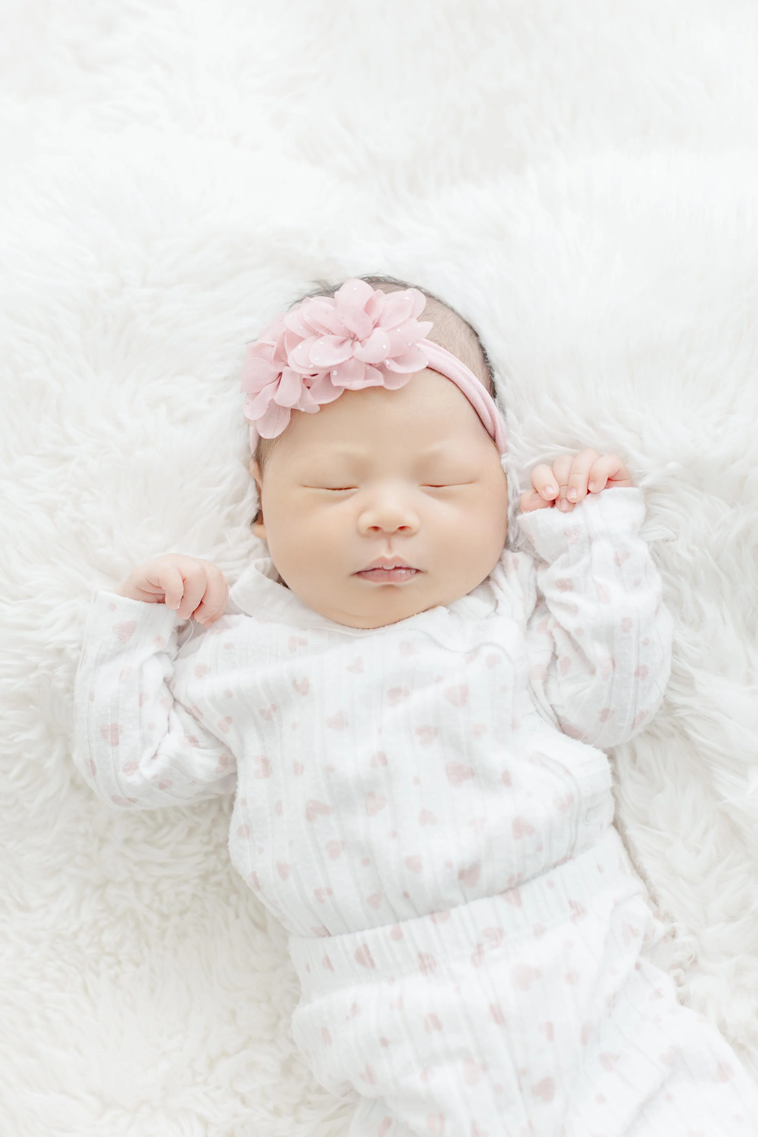 Close-up of a newborn baby girl in a white swaddle with pink headband, fingers curled near her cheek — Greenville SC newborn photographer