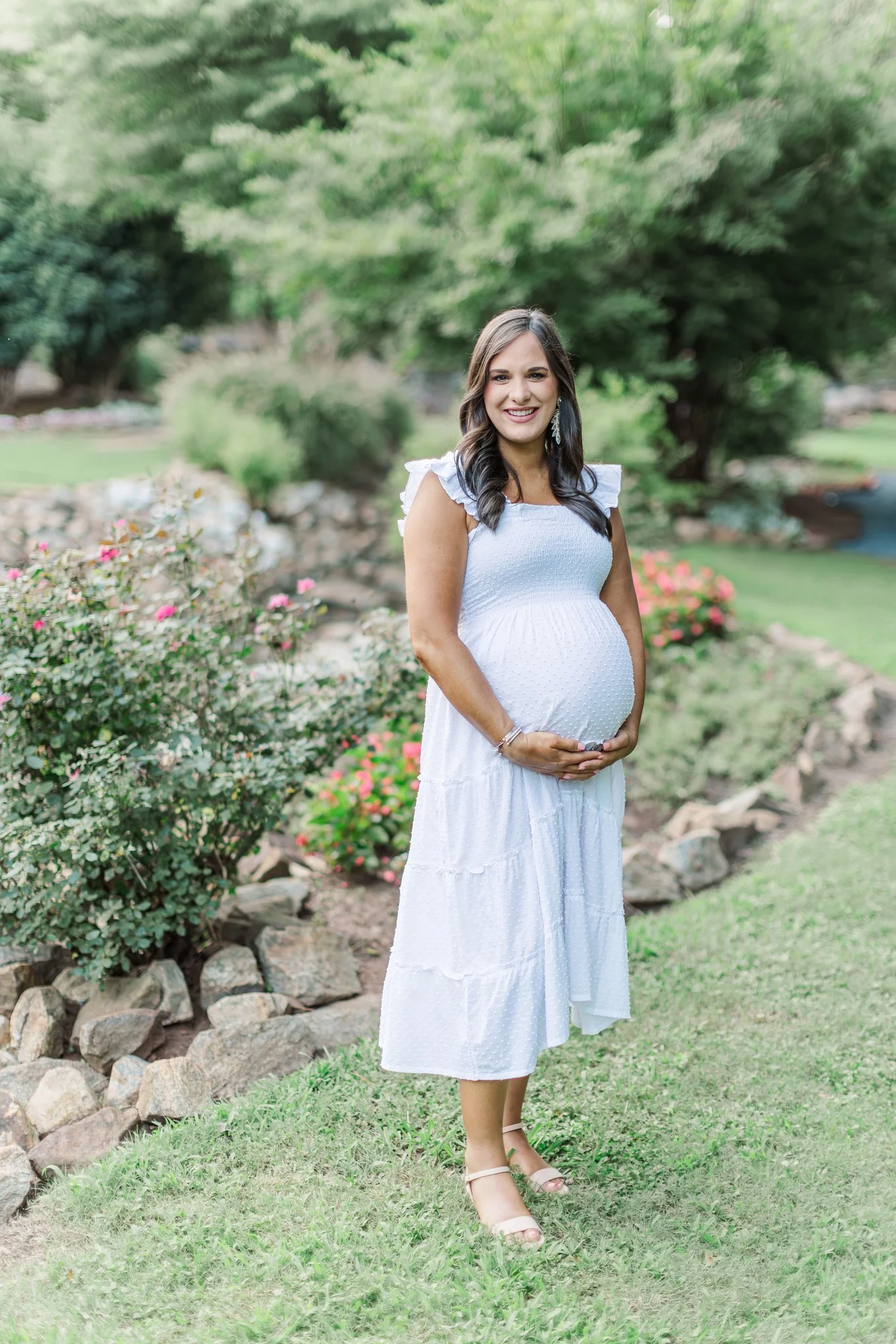 greenville maternity session mom wearing white dress in park with hands holding belly