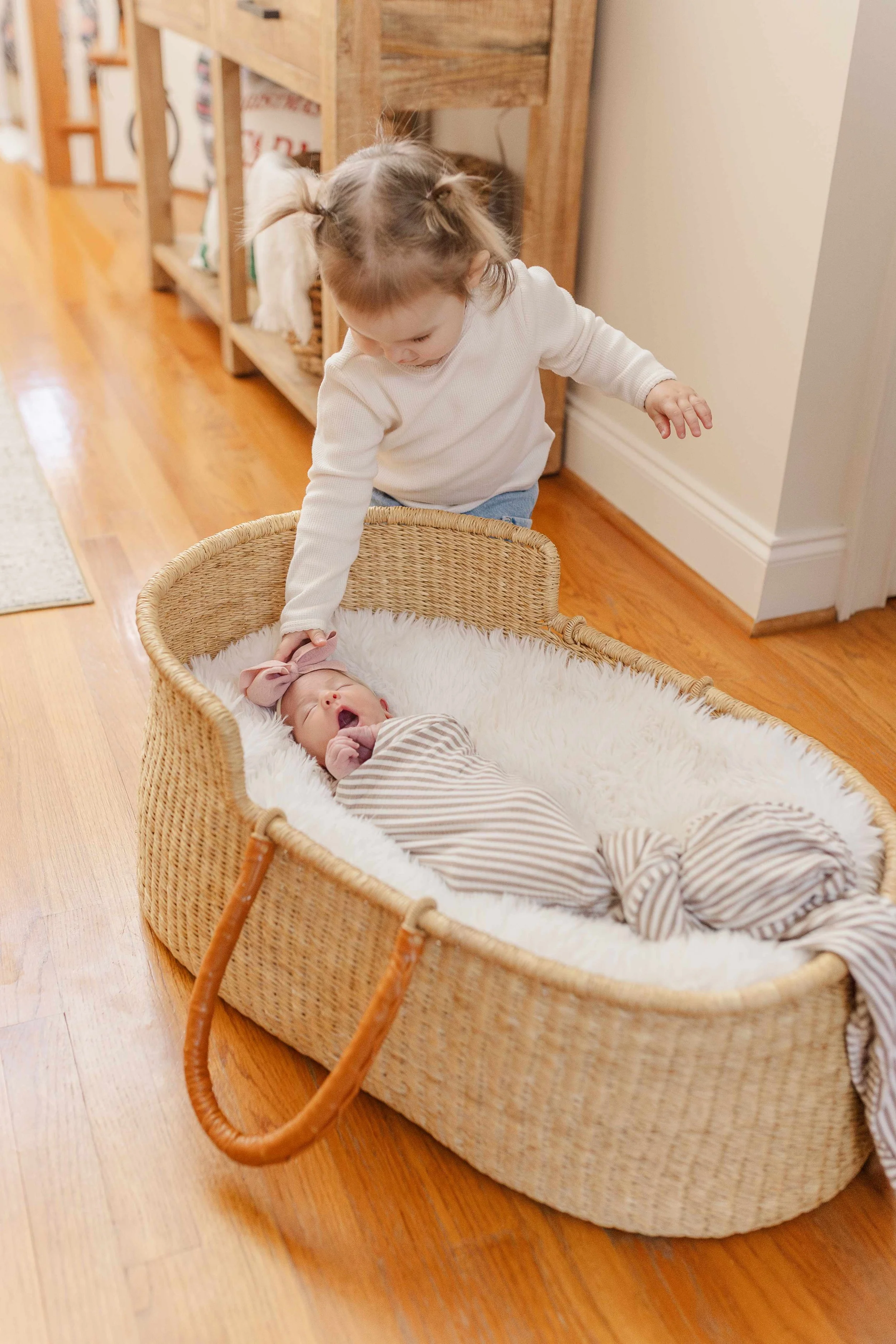 Toddler big sister looking at newborn baby in woven moses basket, sibling newborn photography Easley SC