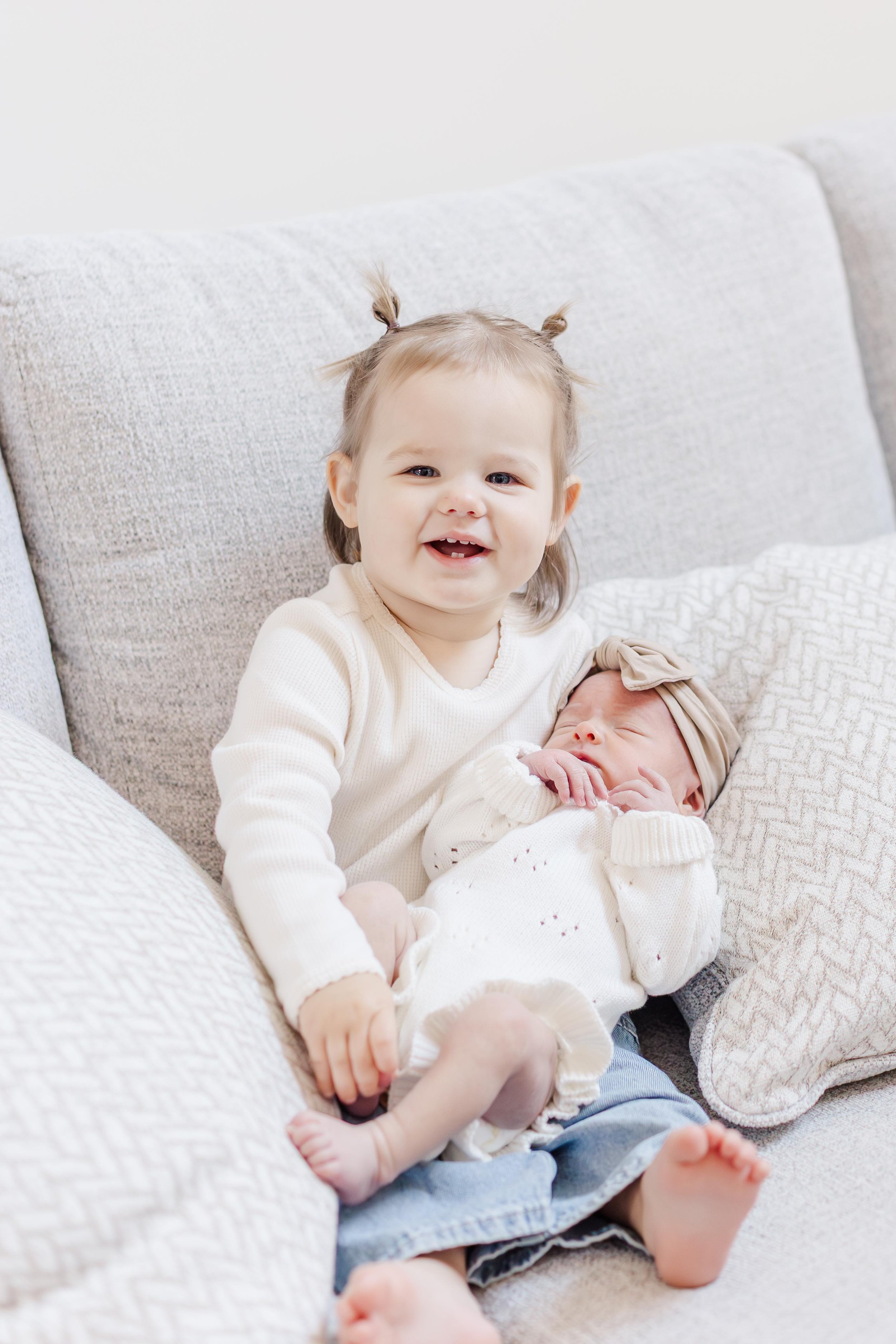 Toddler big sister holding newborn baby sister on couch, sibling newborn photography Easley South Carolina