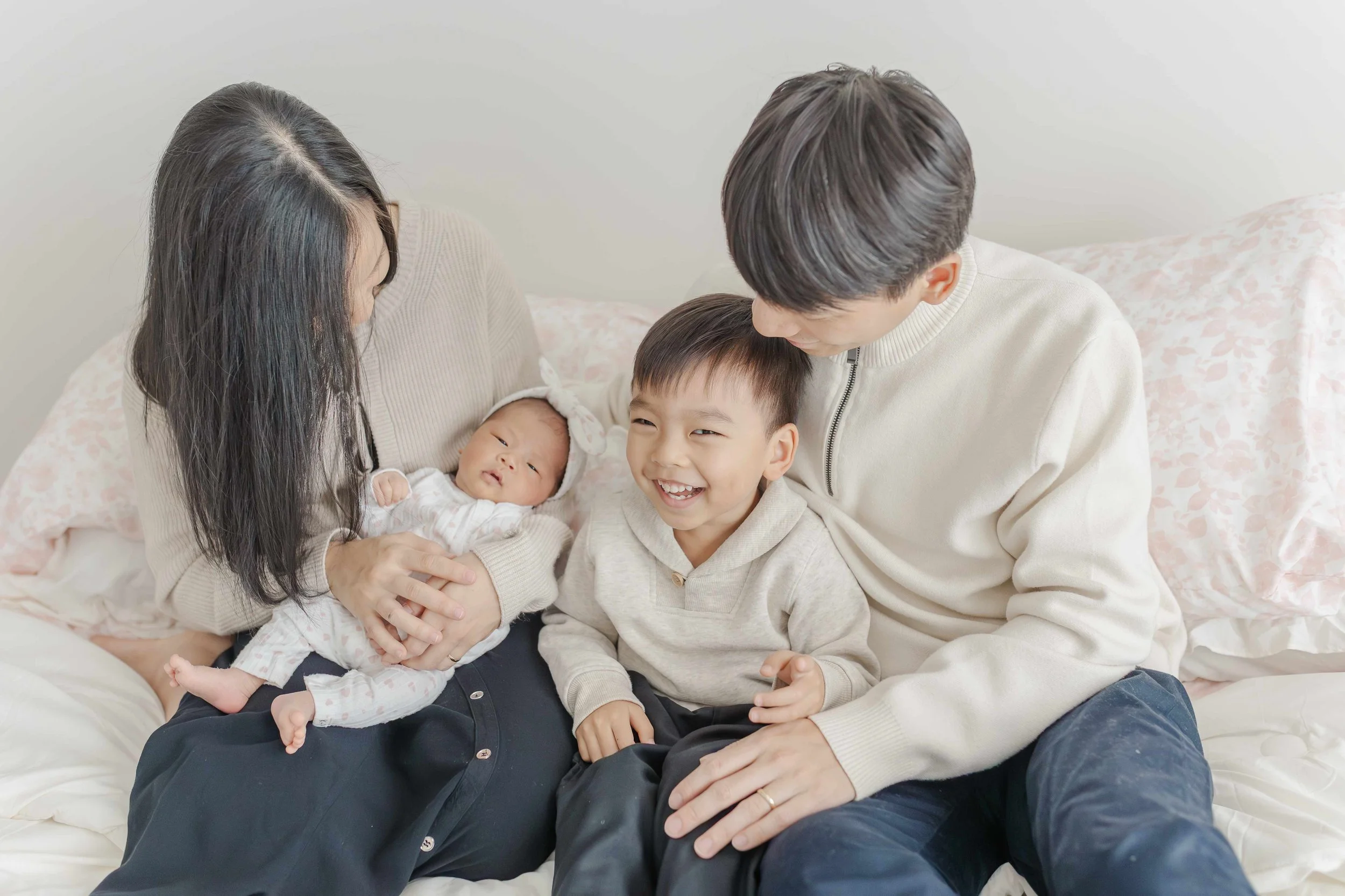 Mom and dad sitting on a white bed with toddler son and newborn baby girl during a lifestyle newborn session in Greenville South Carolina