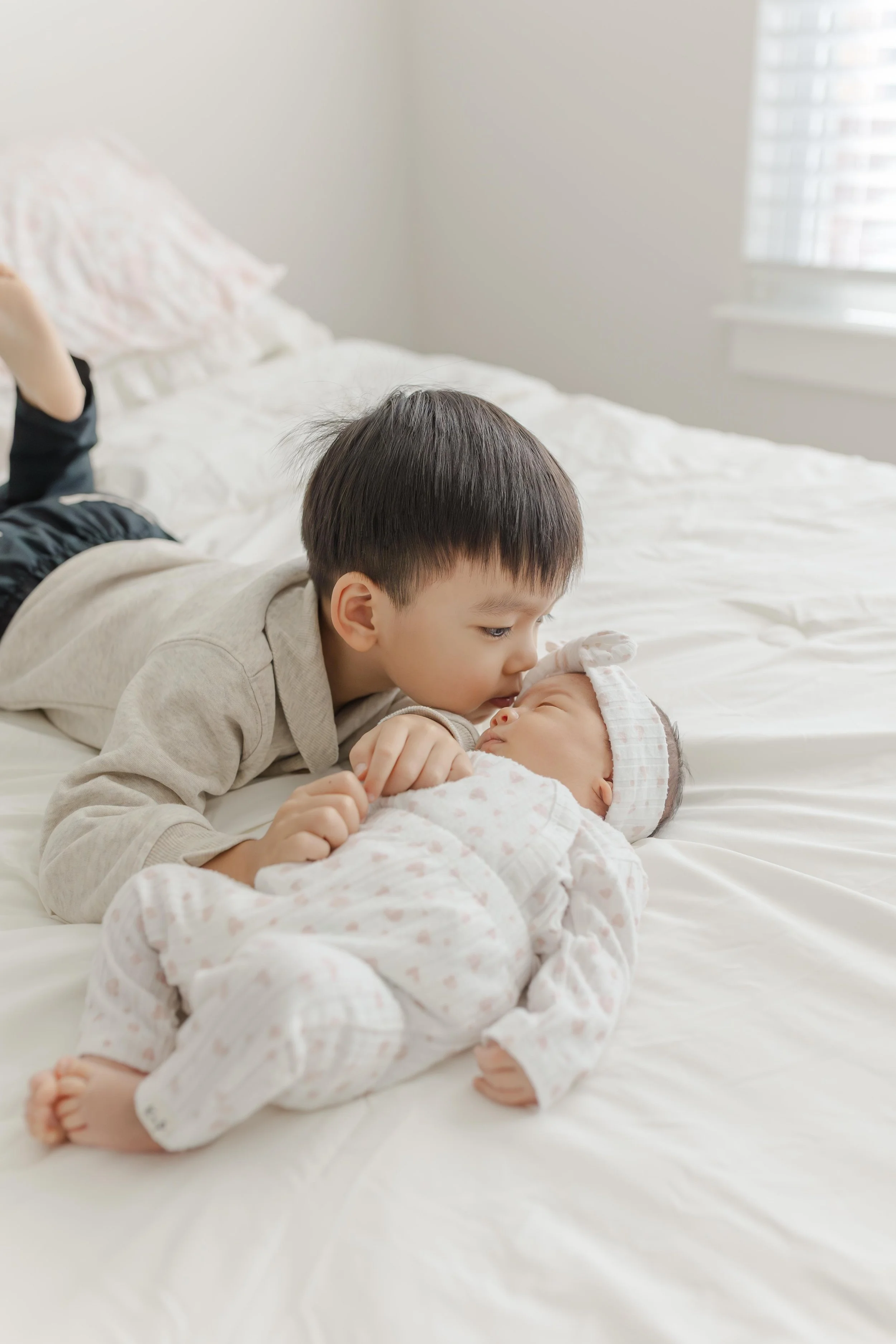 Toddler boy snuggling close to his newborn baby sister on a cream couch — lifestyle newborn photography Greenville South Carolina