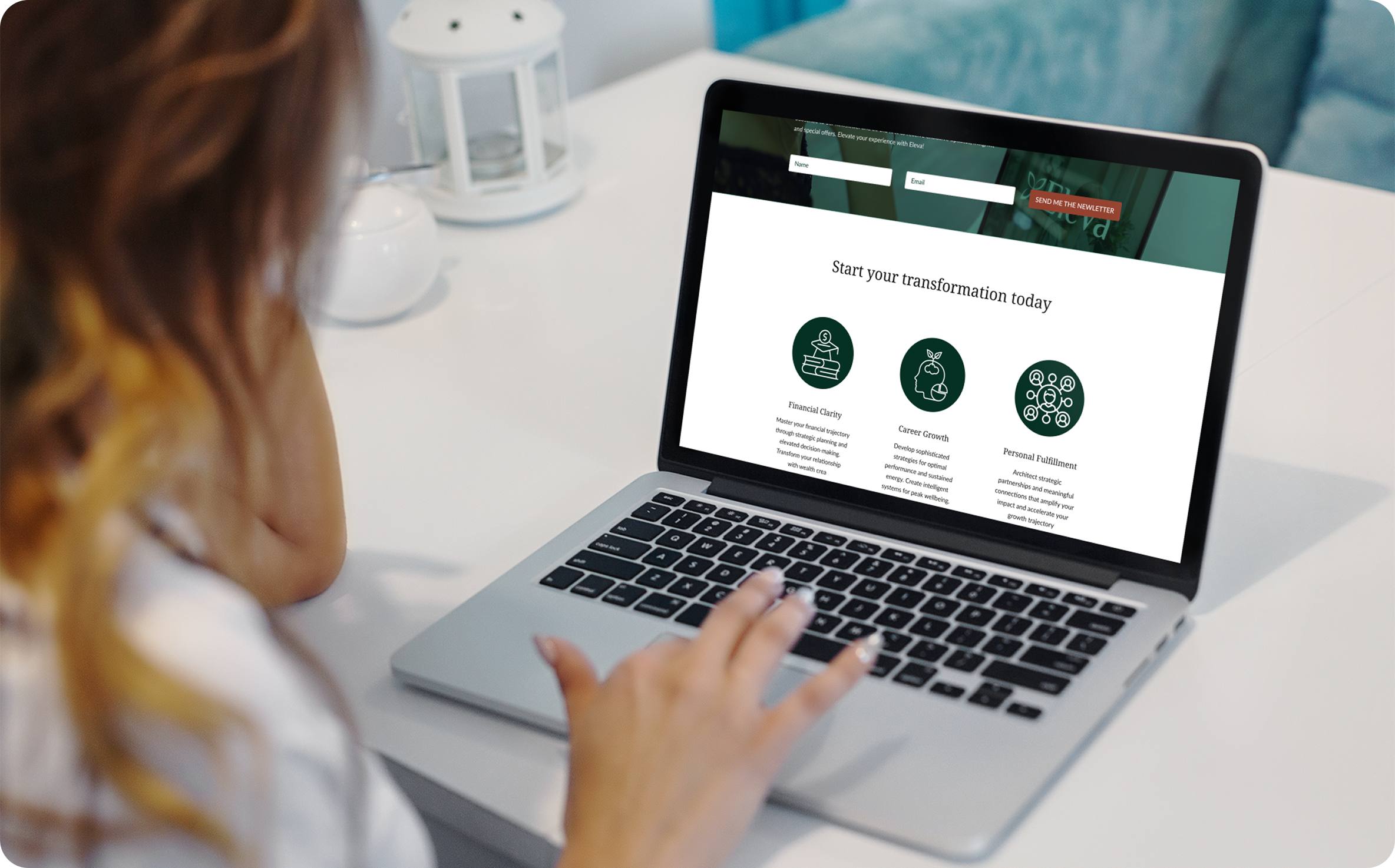 A person with red hair using a laptop to view a website related to personal transformation and coaching. The website features an image slider, a newsletter sign-up form, and section icons with descriptions about financial clarity, career growth, and 