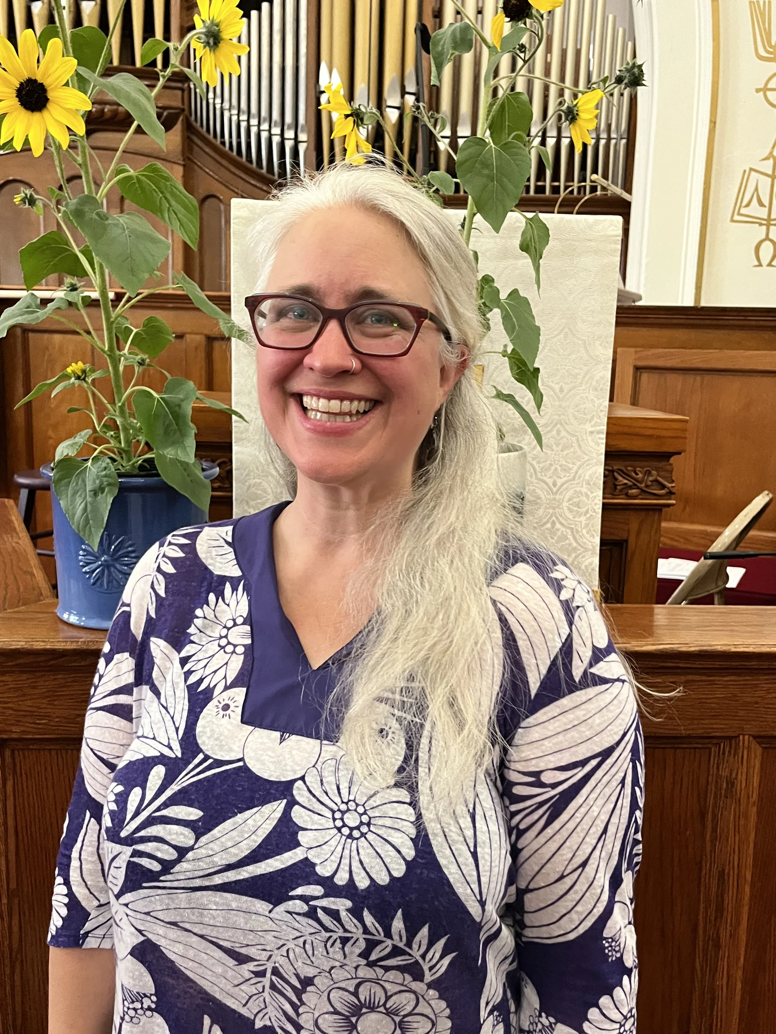 White woman wearing glasses faces the camera and smiles