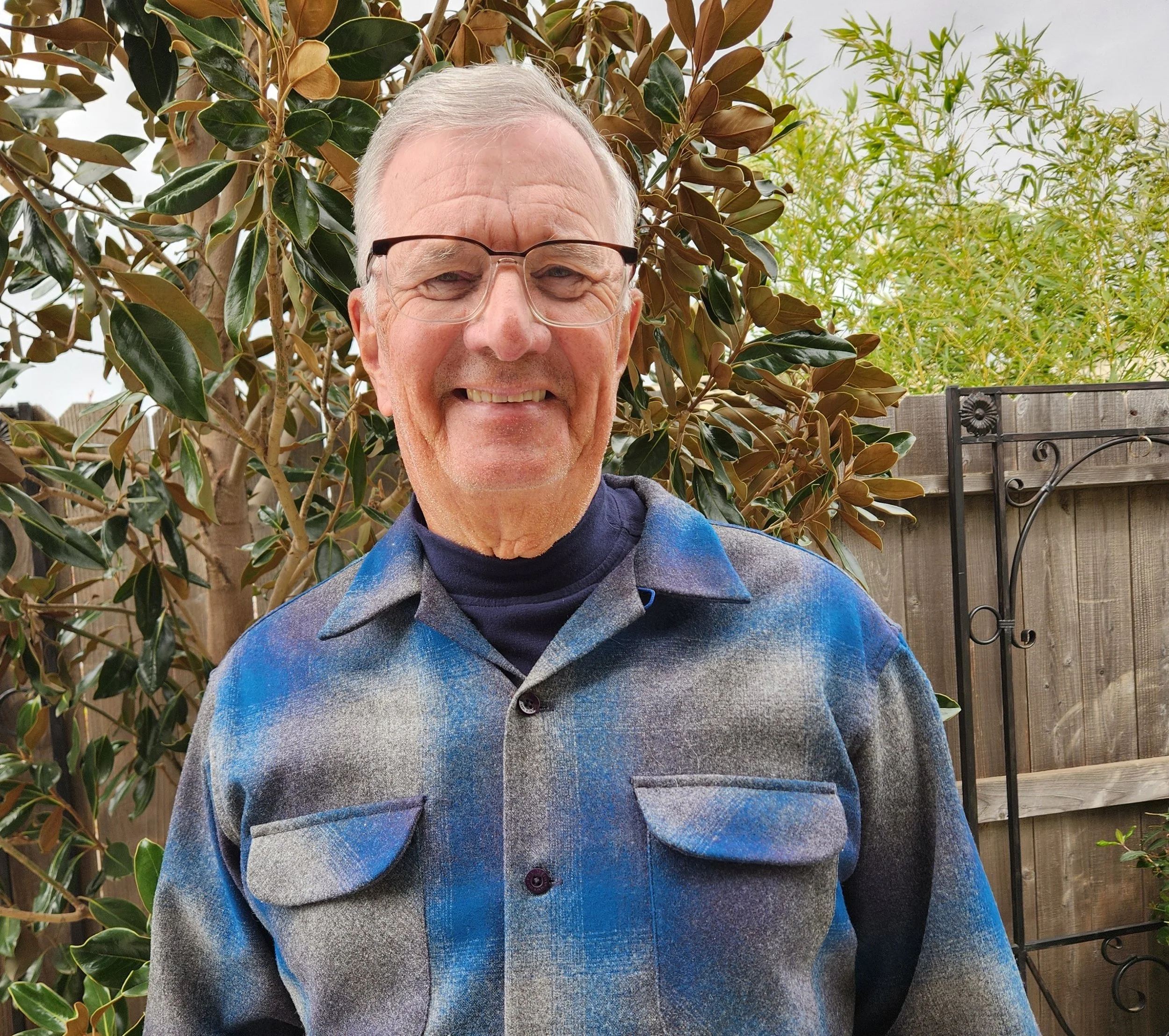 Smiling man wearing a patterned shirt against a plain background.