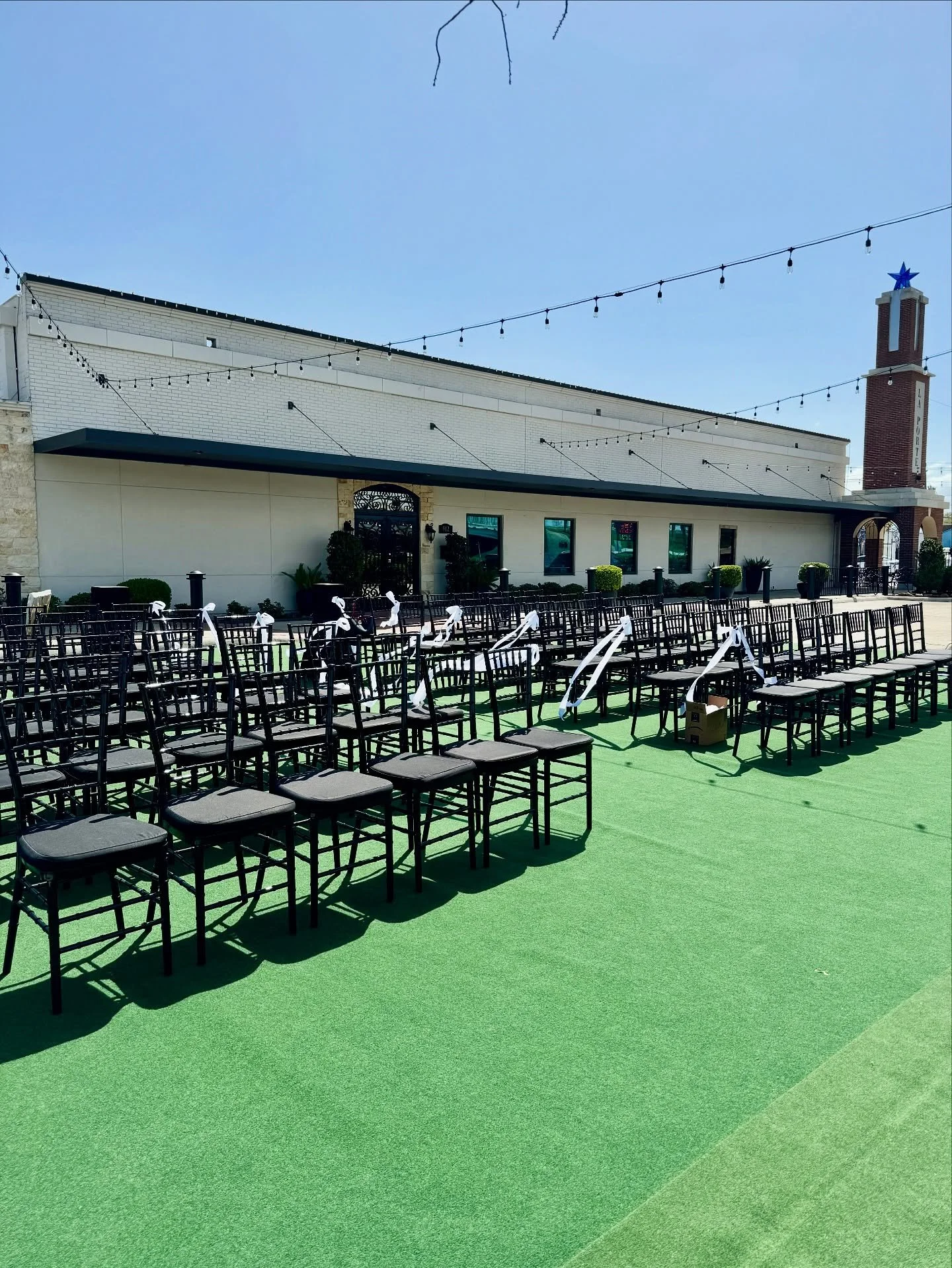 Chic black chairs and white ribbons line the green turf, set beneath string lights for a perfect outdoor ceremony moment ✨💍 #venue #weddings #ceremony #weddinginspiration #venuespace #venuerental #thegatesonmain #outdoorceremony