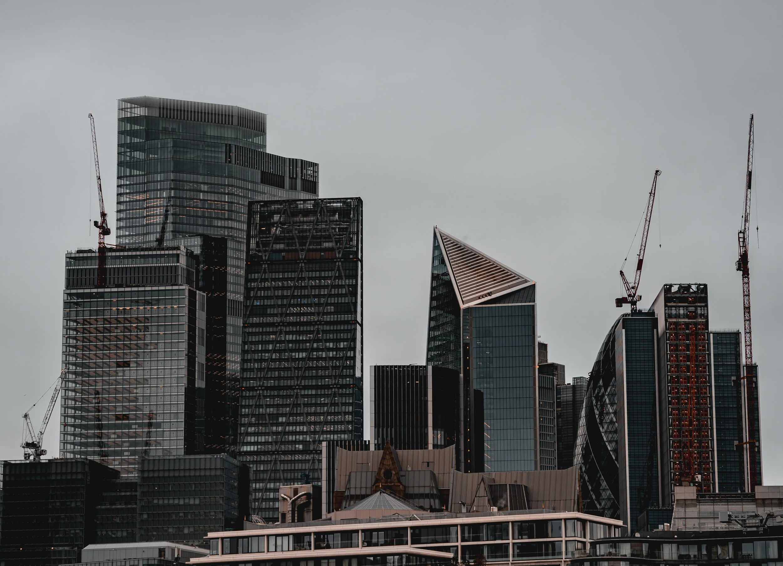 Skyline of modern skyscrapers with cranes in a city, overcast sky.