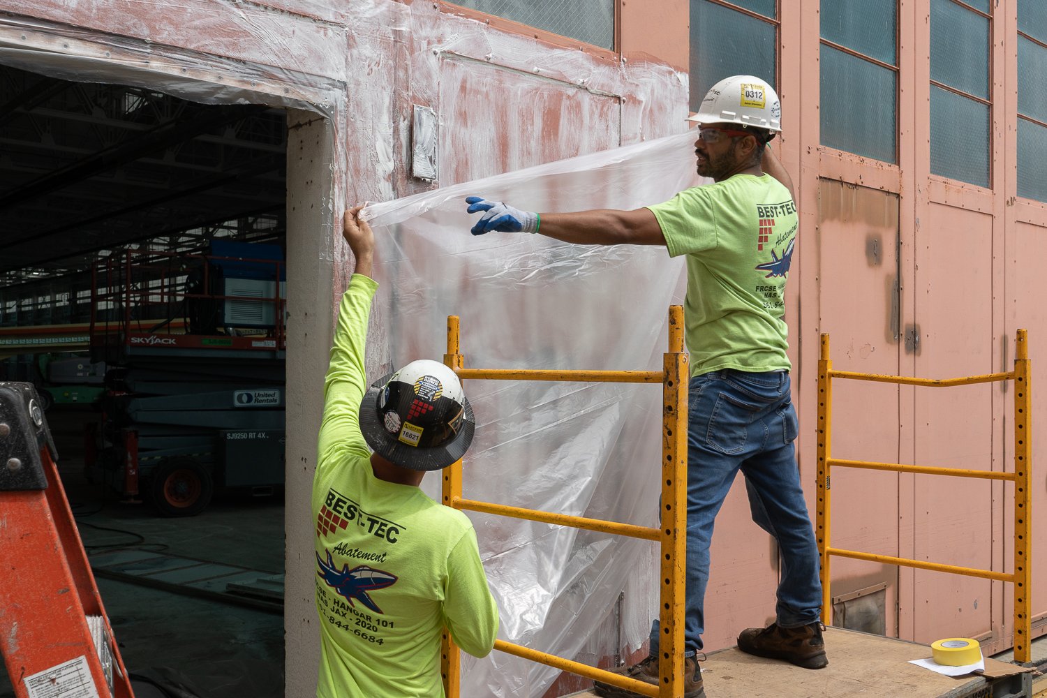 Workers affix a polyethylene sheet so that the paint stripper does not dry out and to reduce exposure of lead paint.