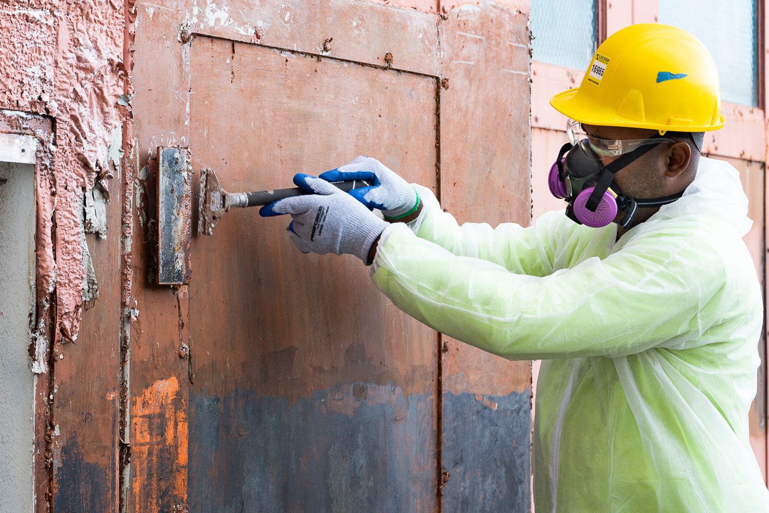 A worker scrapes paint that has a paint stripper applied to it. The next step is to remove the remaining debris using laser ablation.