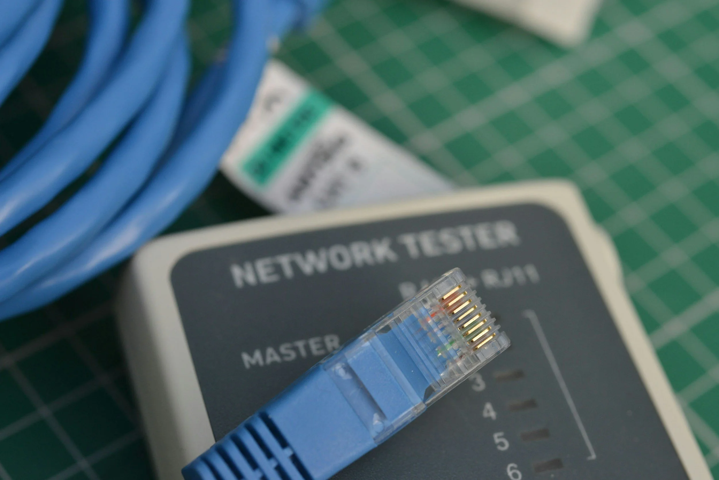 Close-up of a network tester device with an Ethernet cable attached, set on a green cutting mat surface.