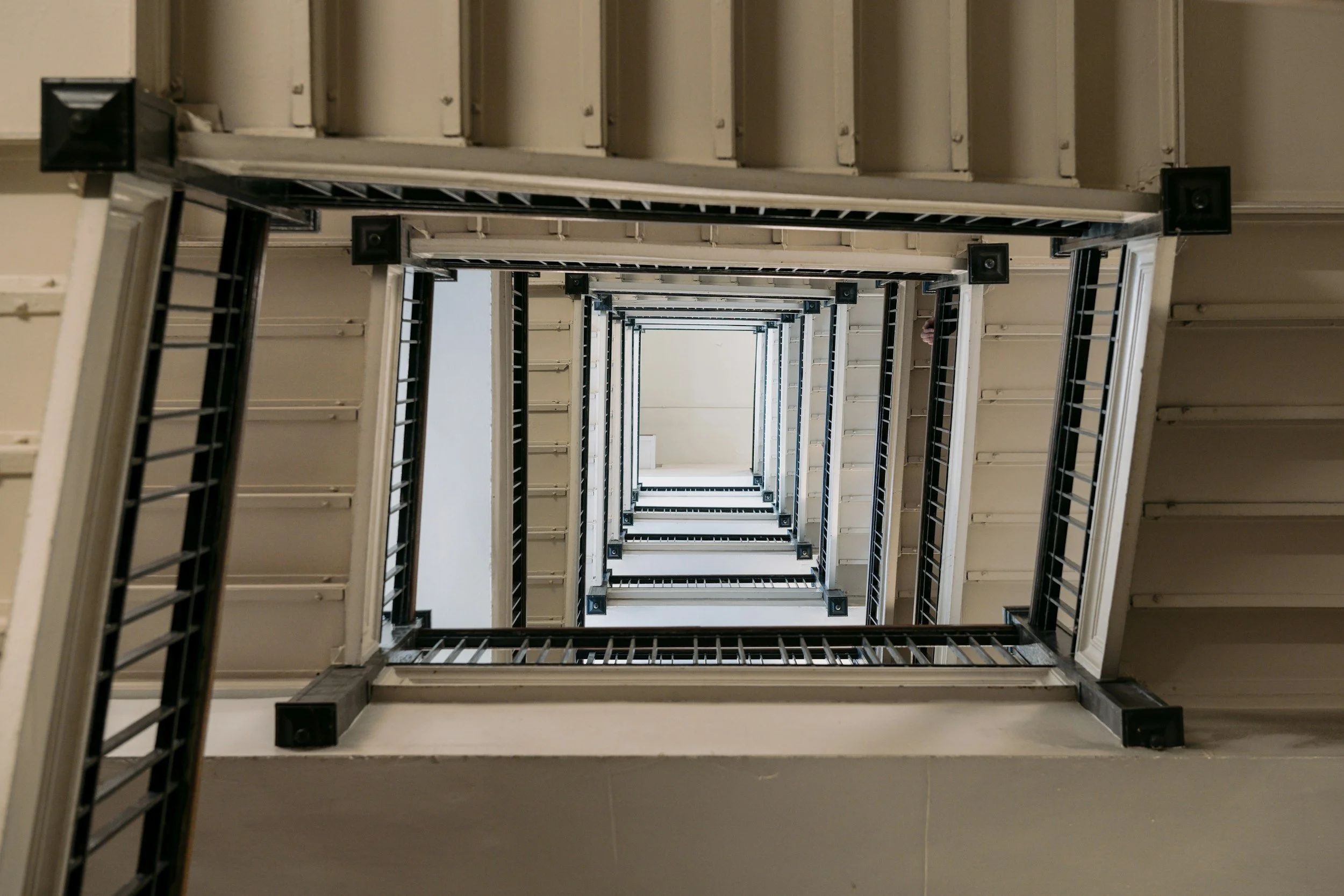 Looking up a vertical staircase at multiple floors, with railings and speakers visible on each level, creating a spiral-like view.