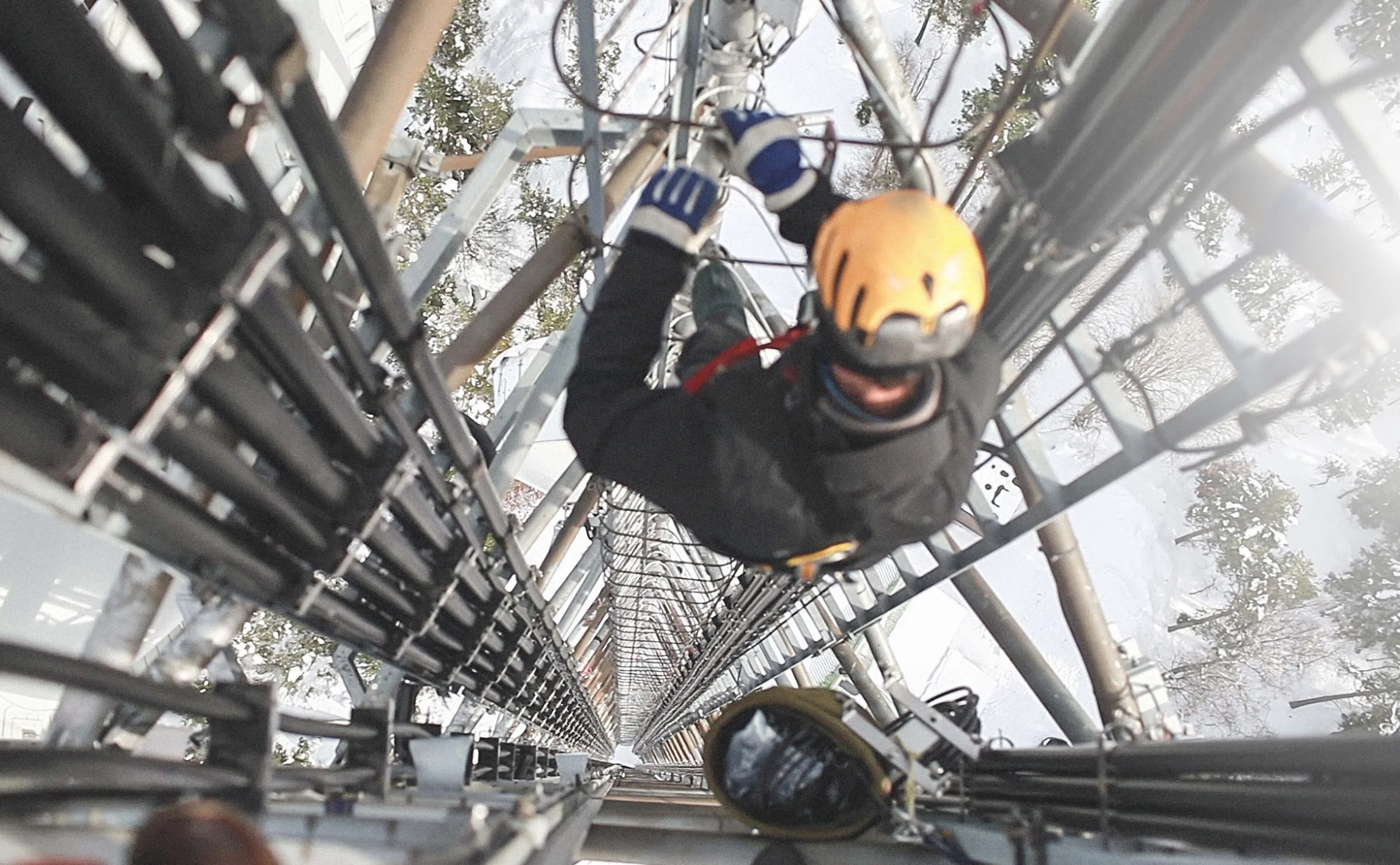 A construction worker climbs a cell phone tower in a snow-covered area.