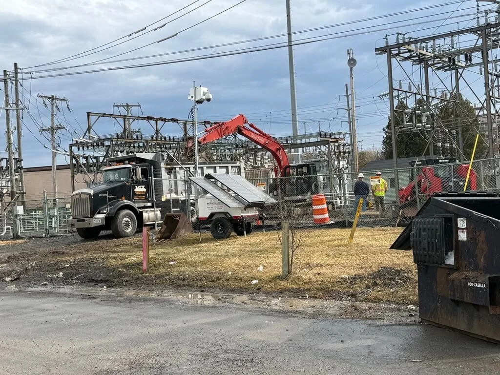 Workers in safety vests and helmets repairing electrical infrastructure at a power substation.
