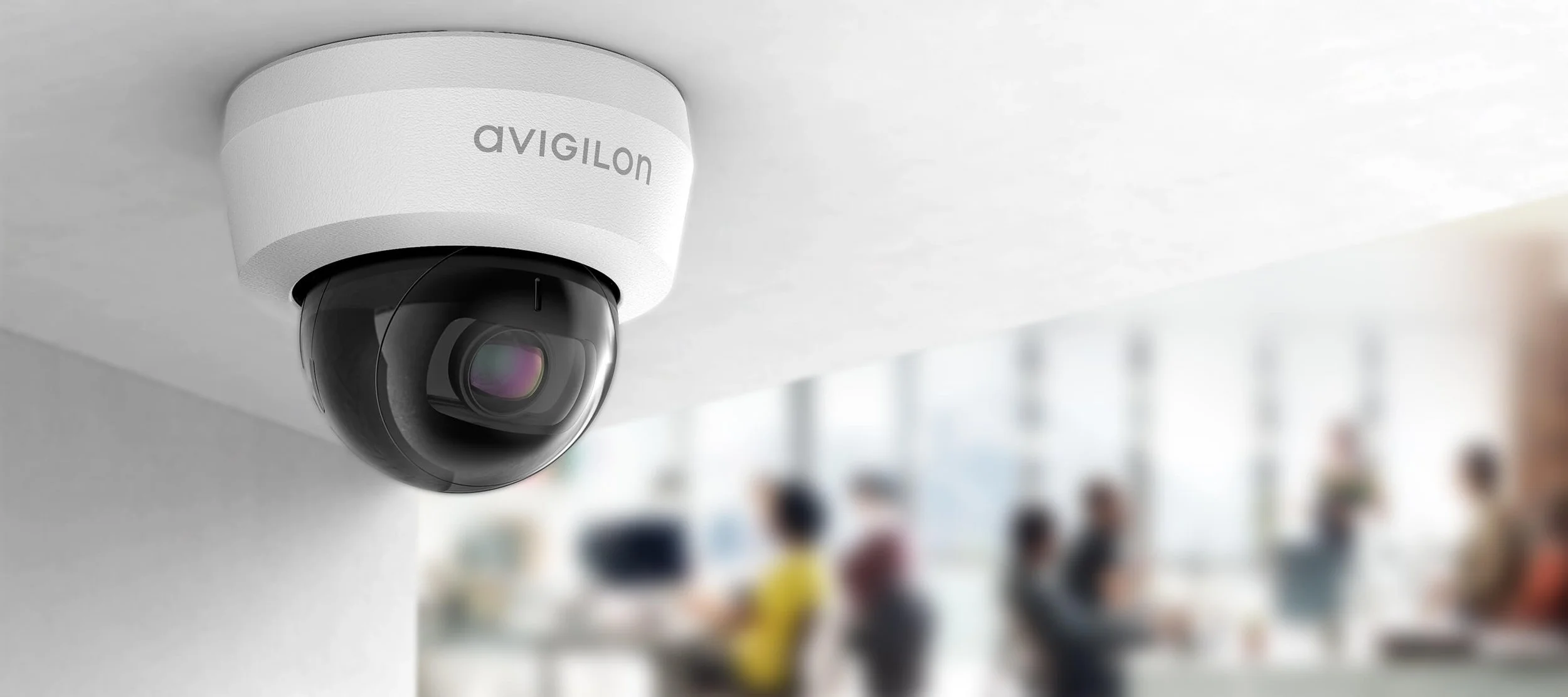 Security camera mounted on ceiling in an indoor space with people blurred in the background.