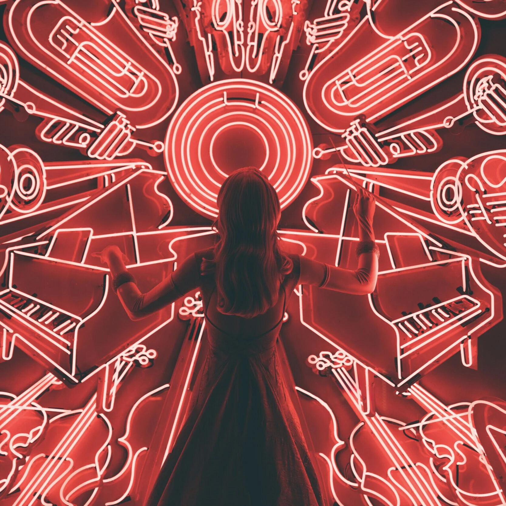 A red image of the silhouette of a woman with her arms in the air conducting. In front of her are neon lights in the shape of instruments..