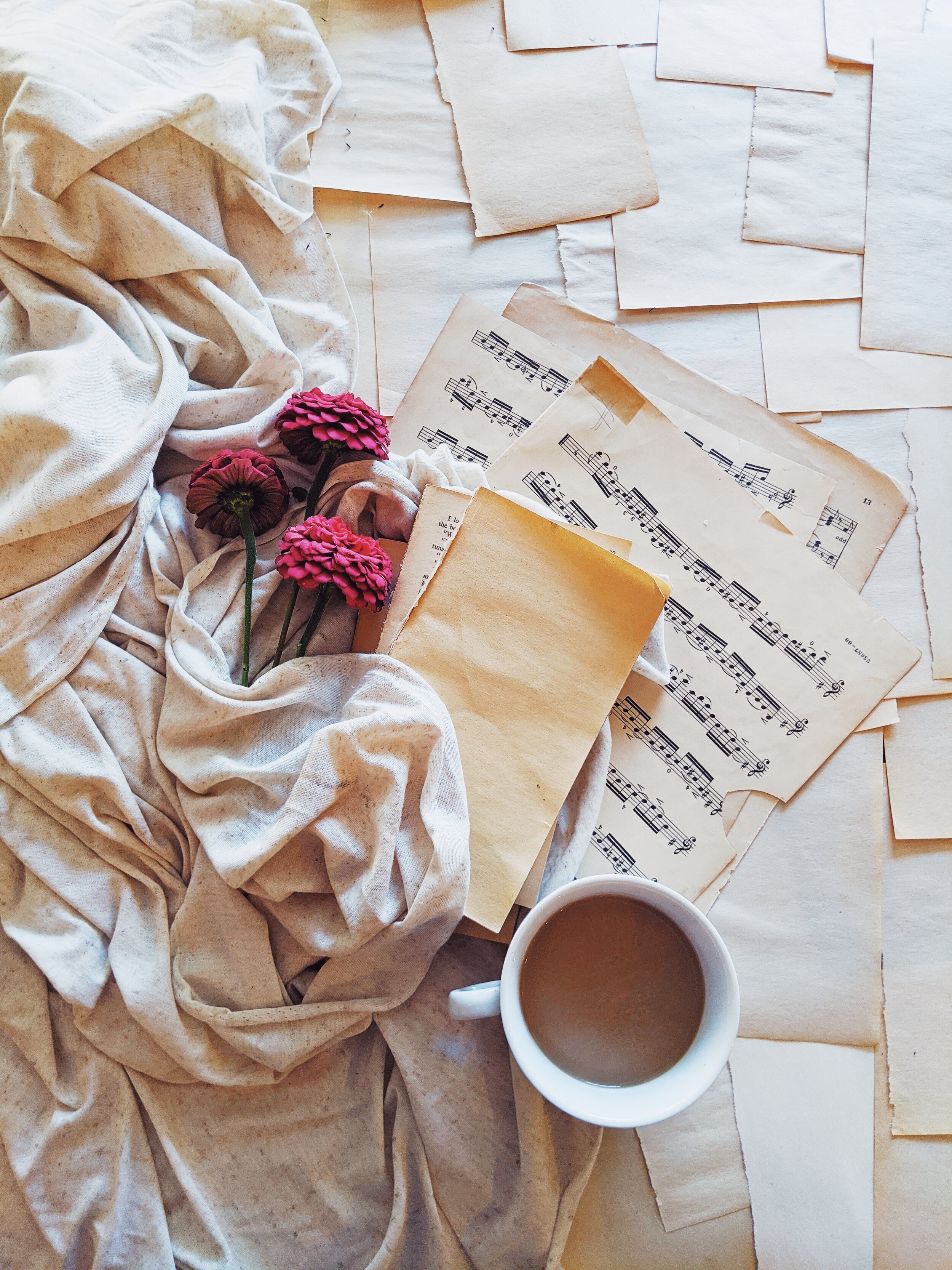 Sheet music, flowers, and fabric with a cup of coffee and cream.