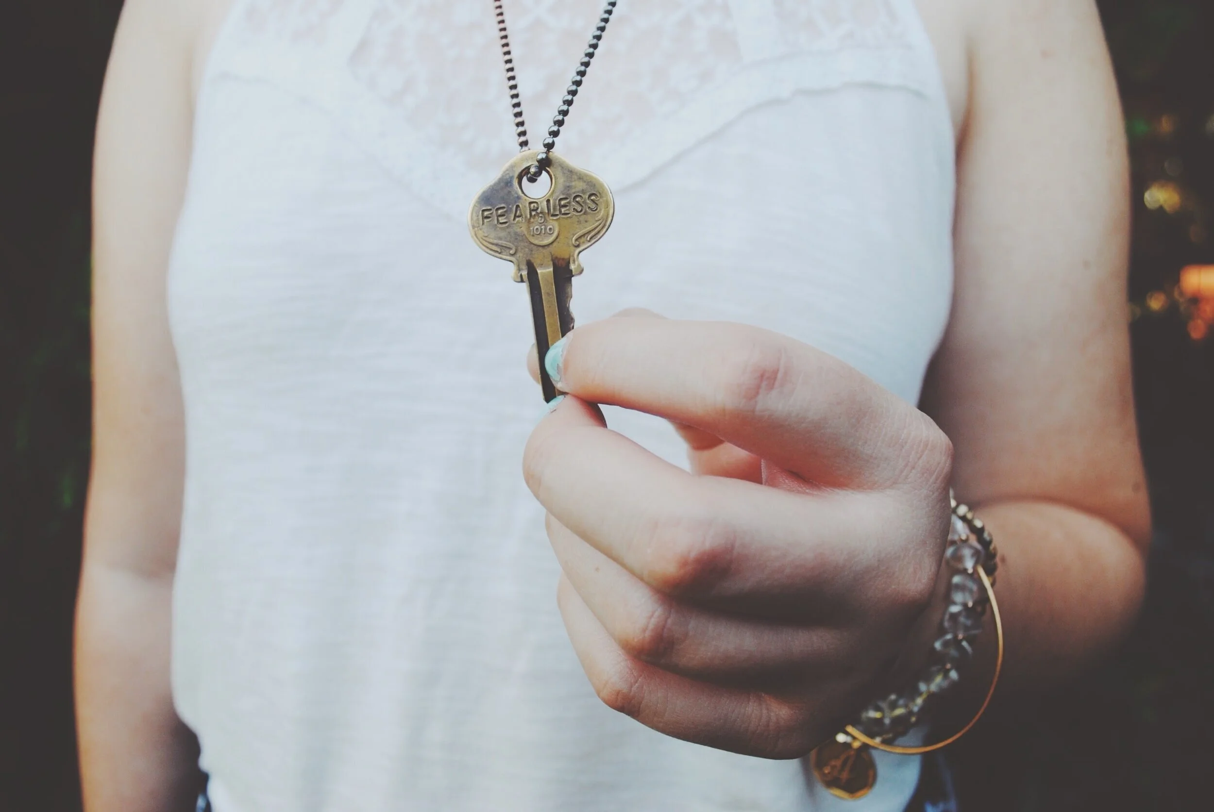 Woman holding a gold key that says fearless attached to a chain hanging around her neck.