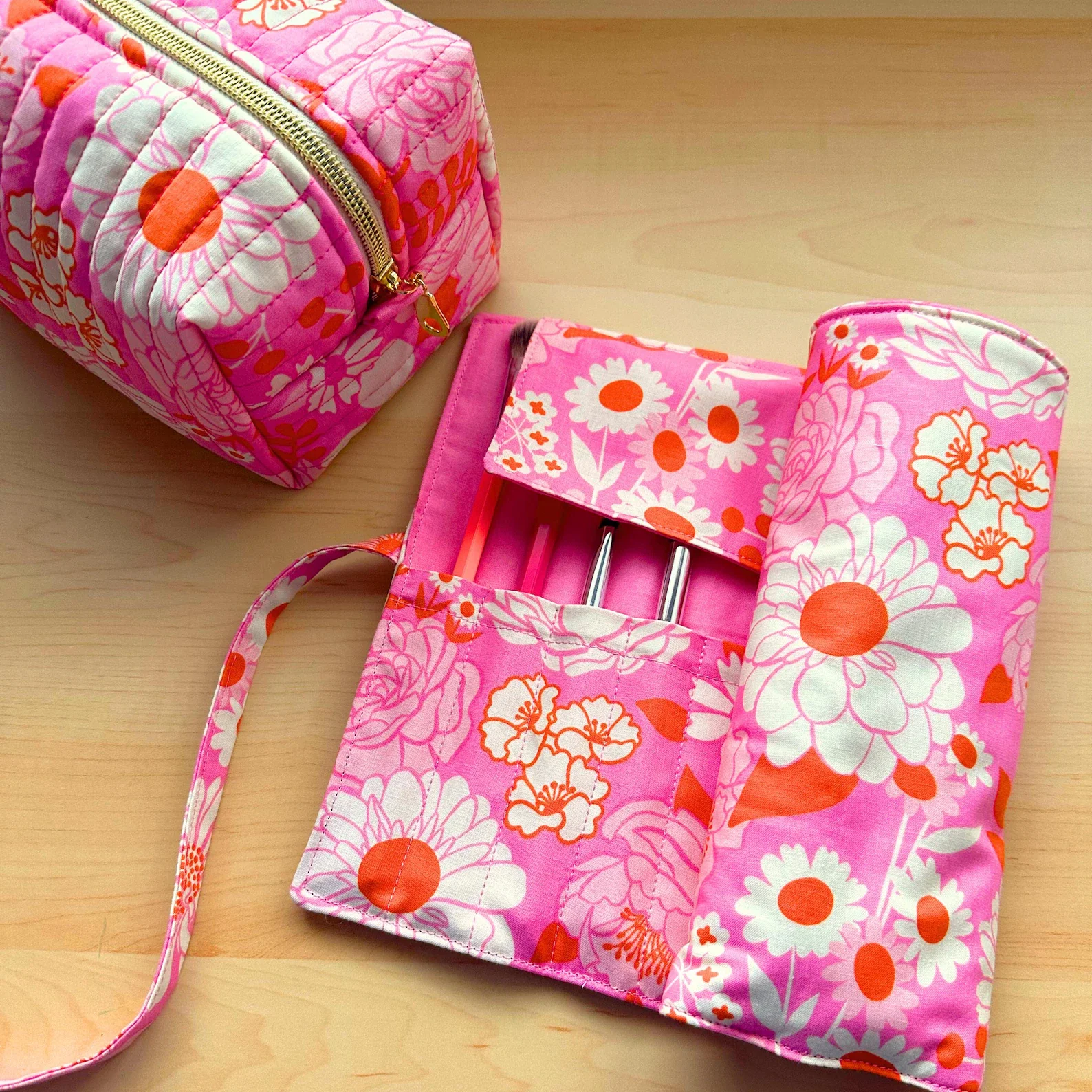A pink fabric makeup or cosmetic bag with a floral pattern, partially open, revealing the inside pocket and some makeup brushes, resting on a wooden surface.