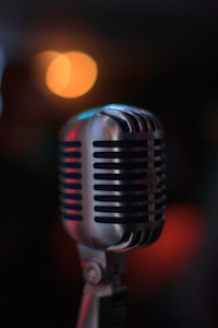 Close-up of a vintage-style microphone against a dark background with blurred orange lights.